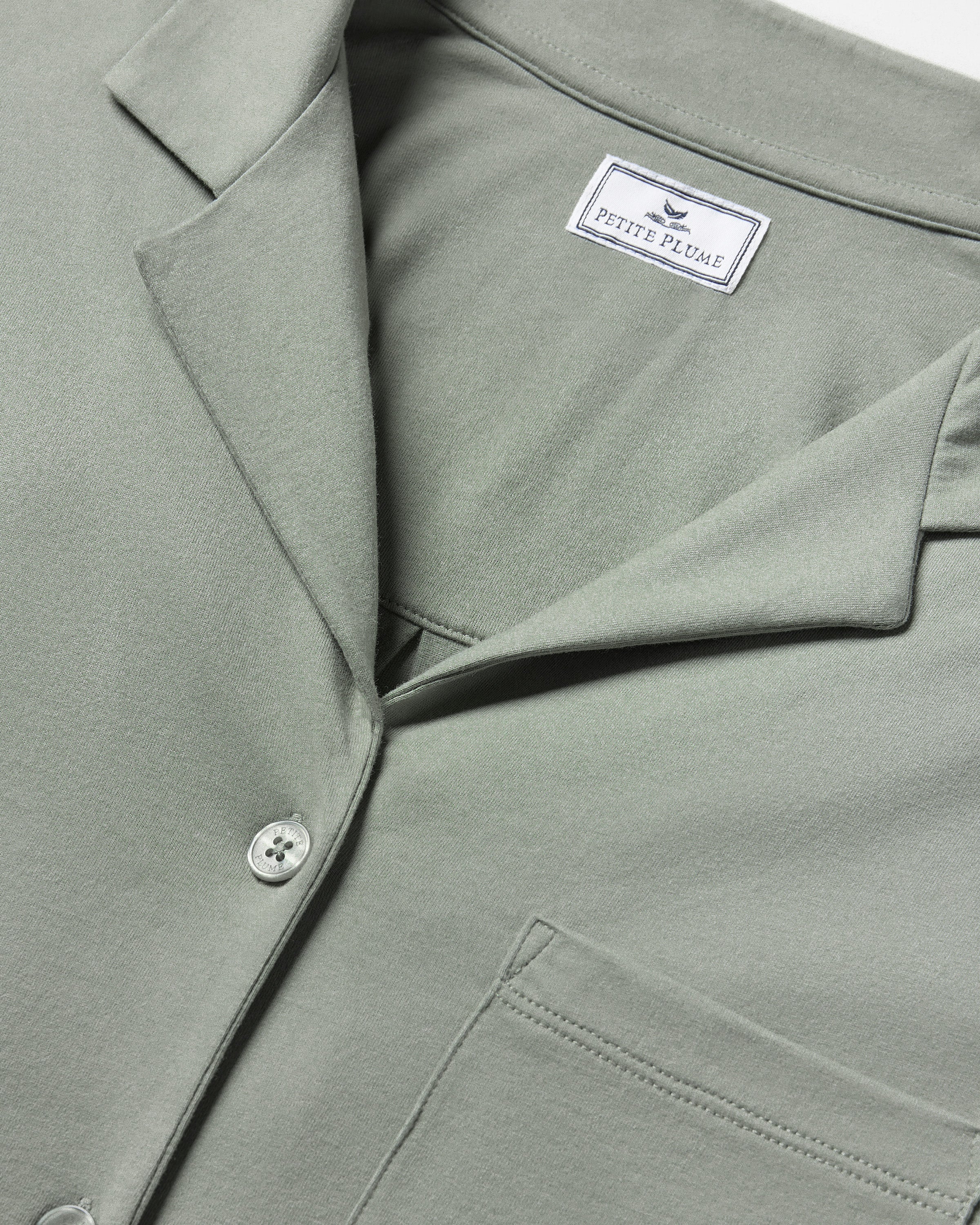 The Olivia Wide Leg Pima Pajama Set in Sage includes a button-up, collared top with a chest pocket and three-quarter sleeves, plus matching elastic waist wide-leg pants. Both pieces are neatly laid flat on a white background.