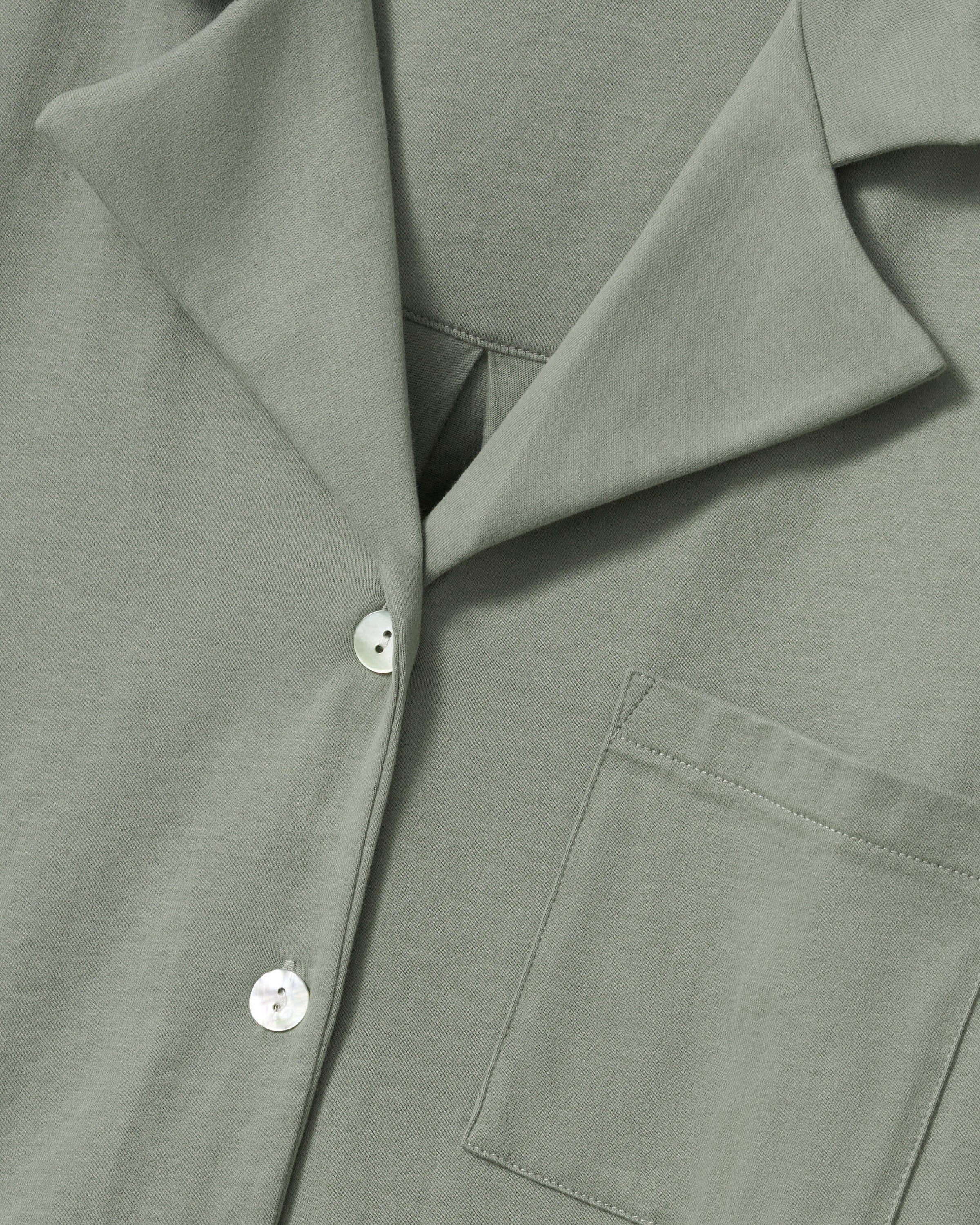 The Olivia Wide Leg Pima Pajama Set in Sage includes a button-up, collared top with a chest pocket and three-quarter sleeves, plus matching elastic waist wide-leg pants. Both pieces are neatly laid flat on a white background.