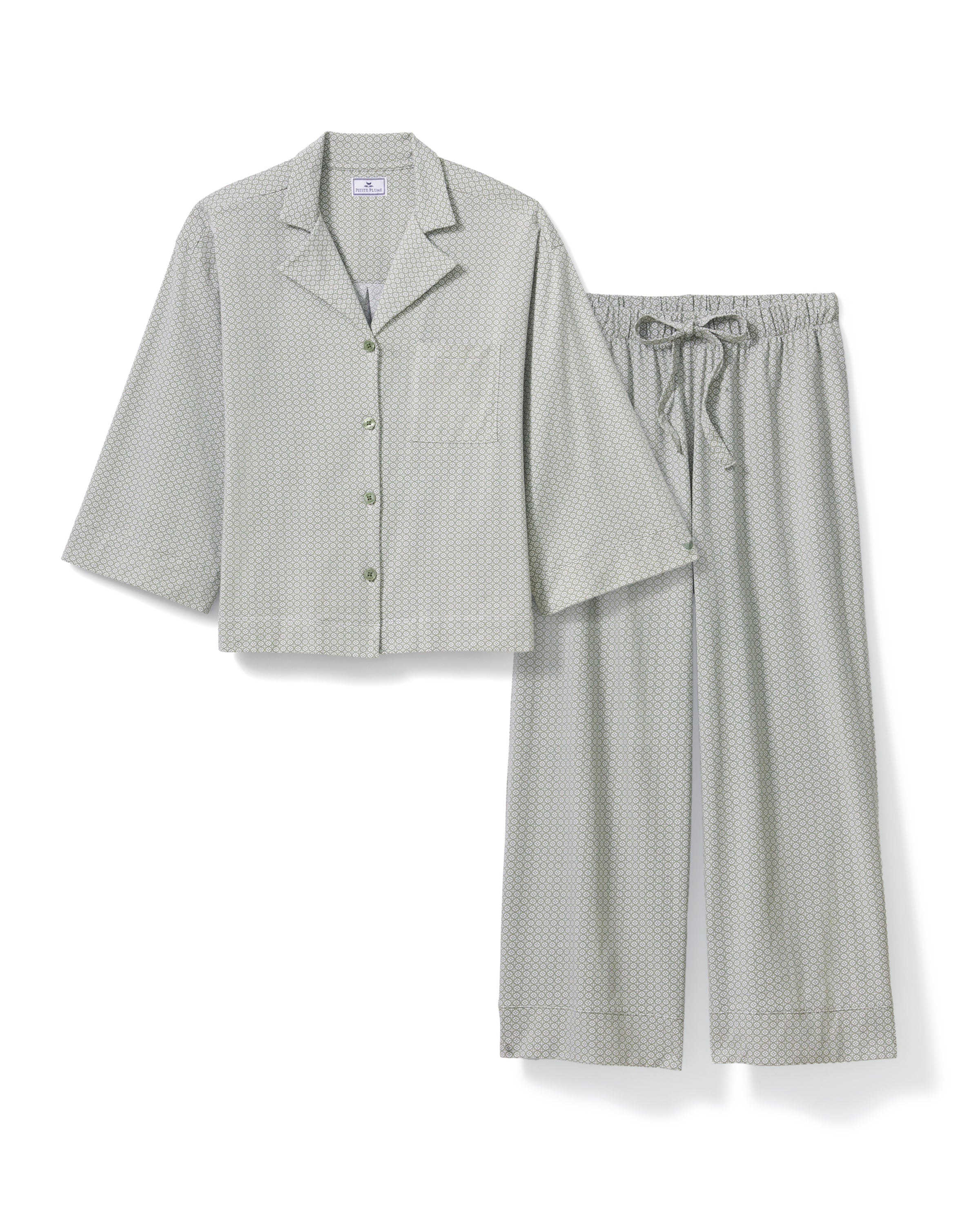 A woman stands barefoot against a plain white background, wearing The Olivia Wide Leg Lightweight Pima Pajama Set in Sage Geo—a matching loose-fitting ensemble with long sleeves and wide-leg pants in a subtle light pattern.
