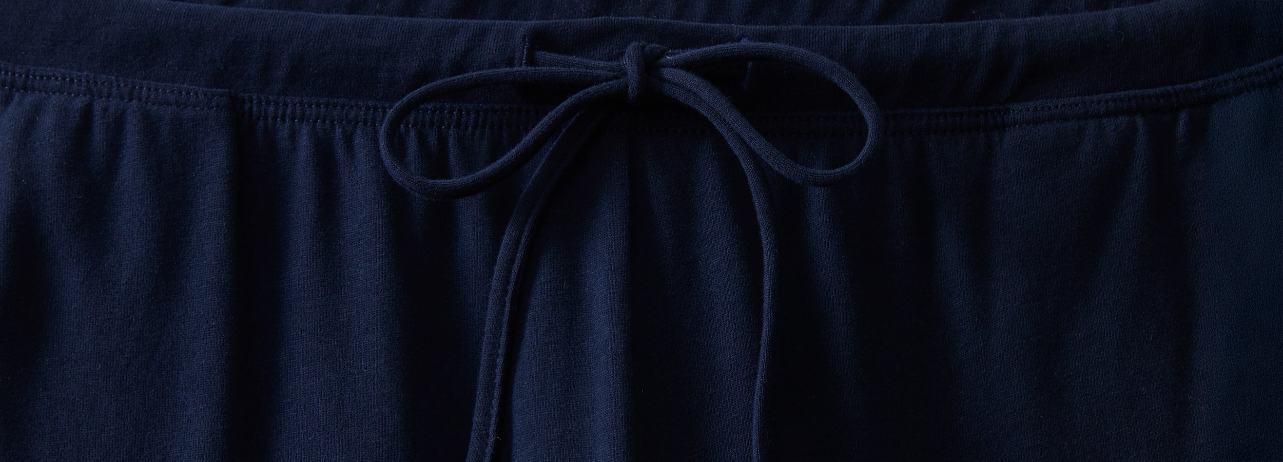 Close-up of a navy blue drawstring waistband, tied in a neat bow, on a fabric garment such as sweatpants or pajama pants.