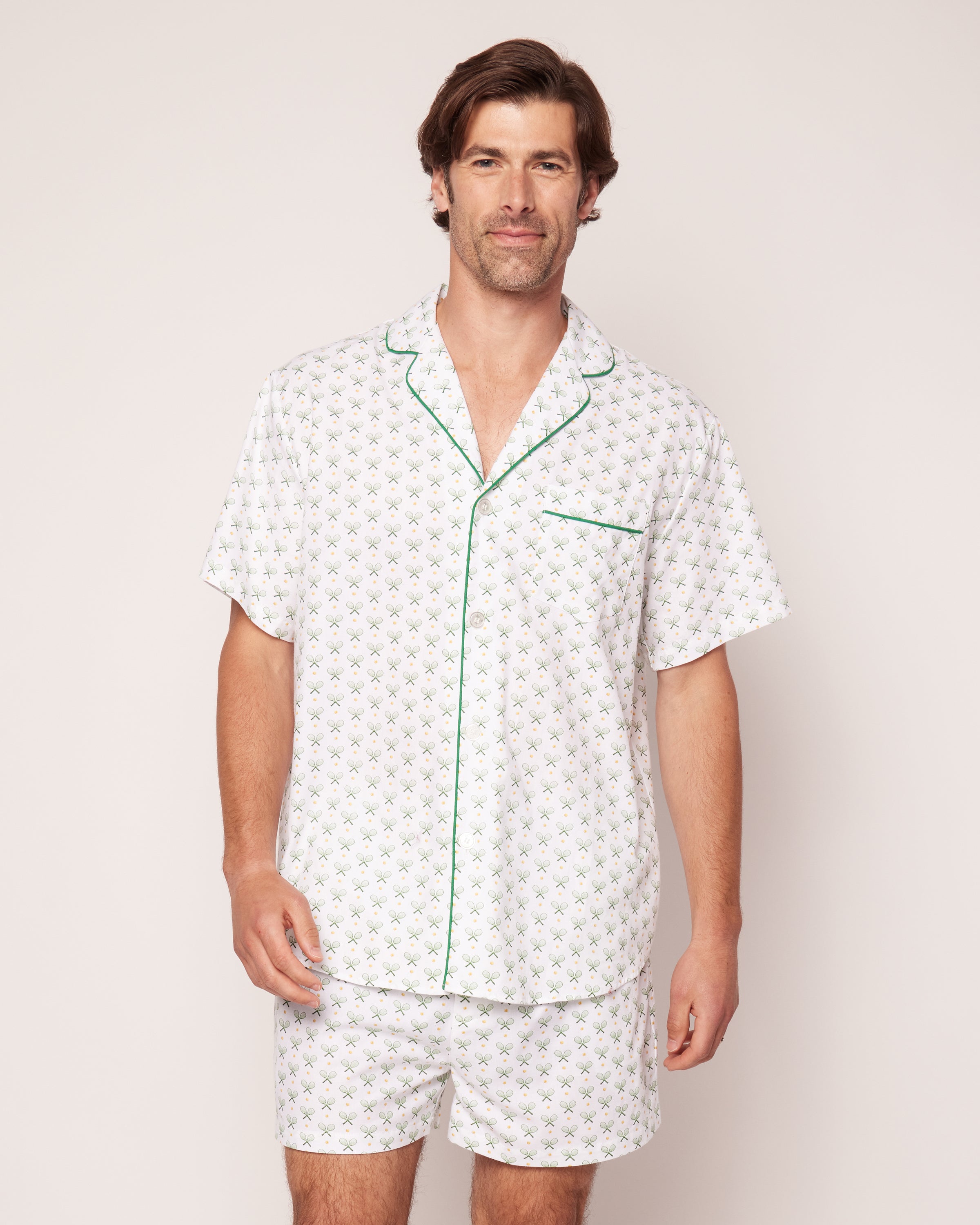 A person is wearing the Mens Twill Pajama Short Set in Match Point by Petite Plume, featuring a small green leaf pattern on 100% cotton with luxurious green piping on the collar and pocket against a white background.