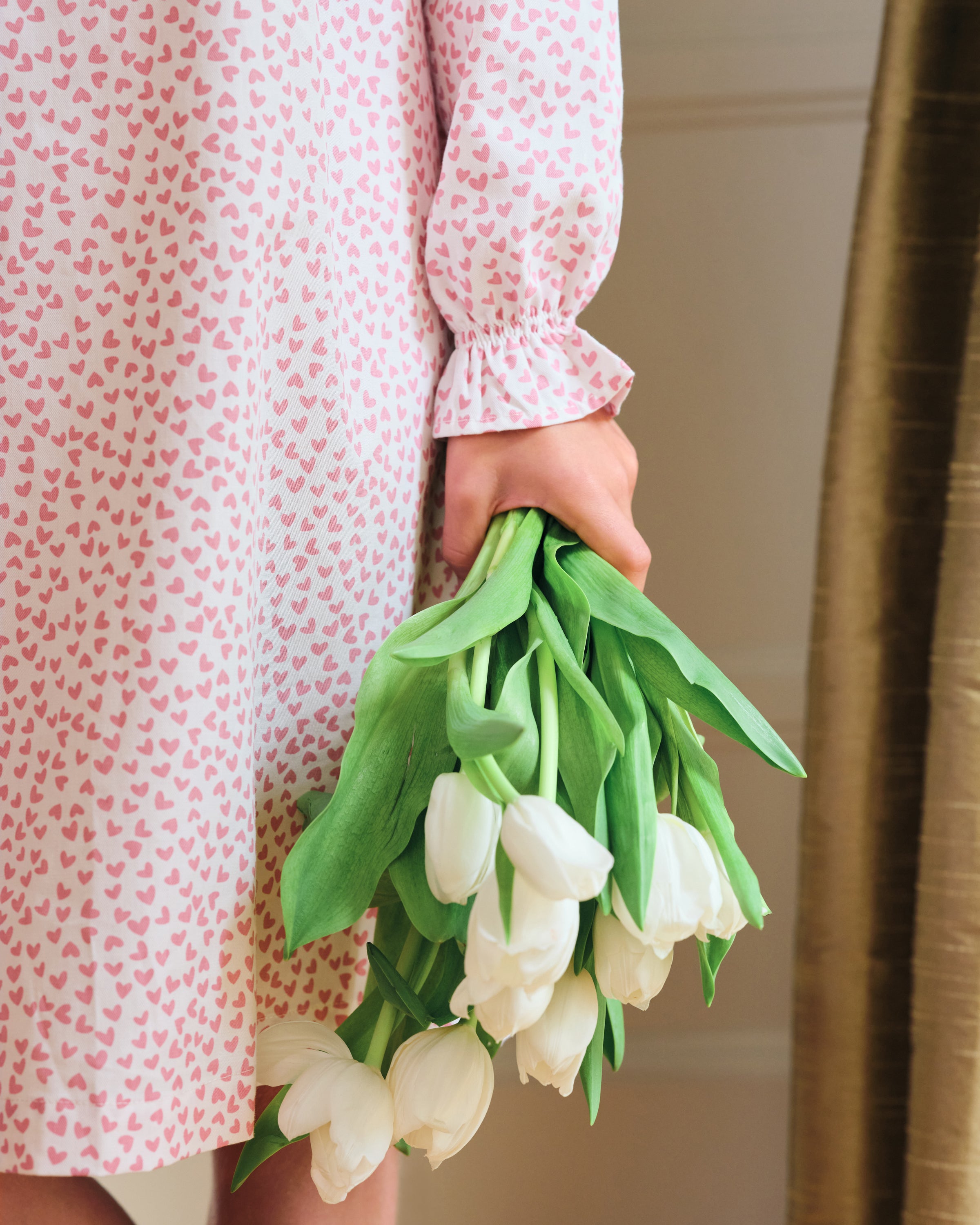 The Girls Twill Delphine Nightgown in Sweethearts by Petite Plume features long sleeves, white fabric with a pink floral pattern, is made from yarn-dyed cotton, and has a ruffled neckline with a small bow and ruffled sleeve cuffs.