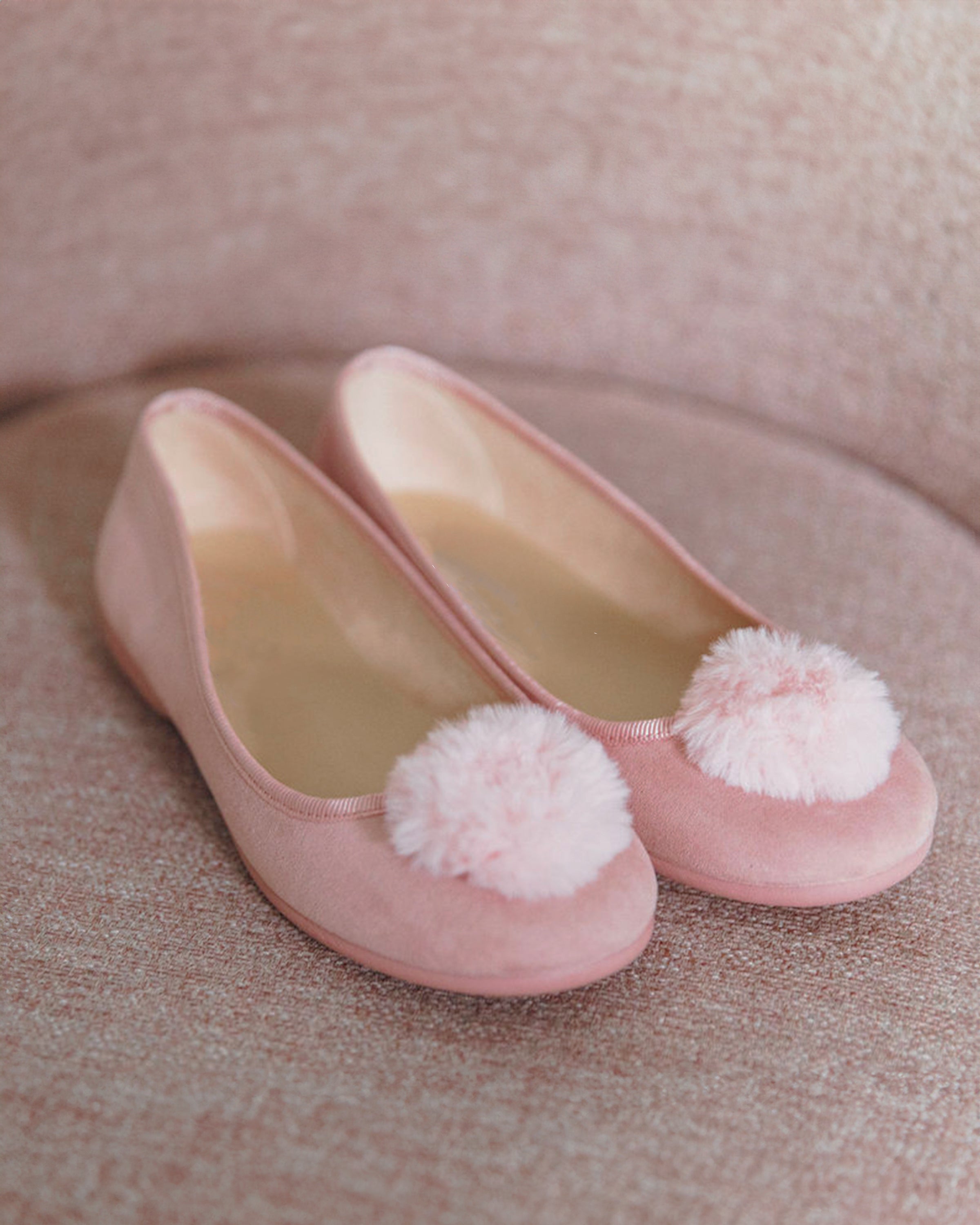 The Kids Juliette Slipper by Petite Plume in antique rose suede features festive pom-poms on the toes, set against a matching pink textured surface.