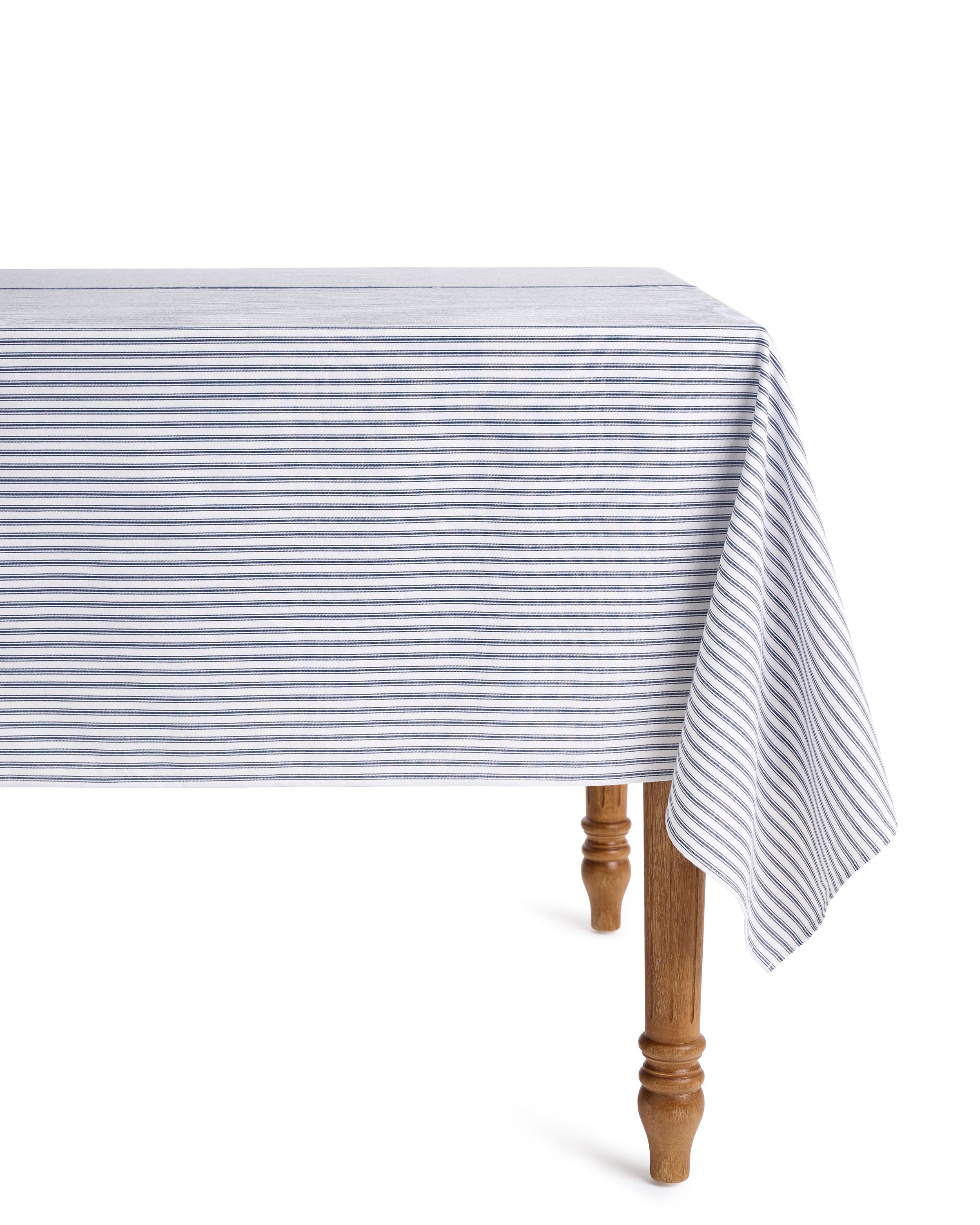 A wooden table adorned with the Signature Twill Tablecloth in Navy French Ticking by Petite Plume drapes elegantly over the sides, highlighting its ornate legs. This simple yet festive setting creates a well-lit and inviting ambiance.