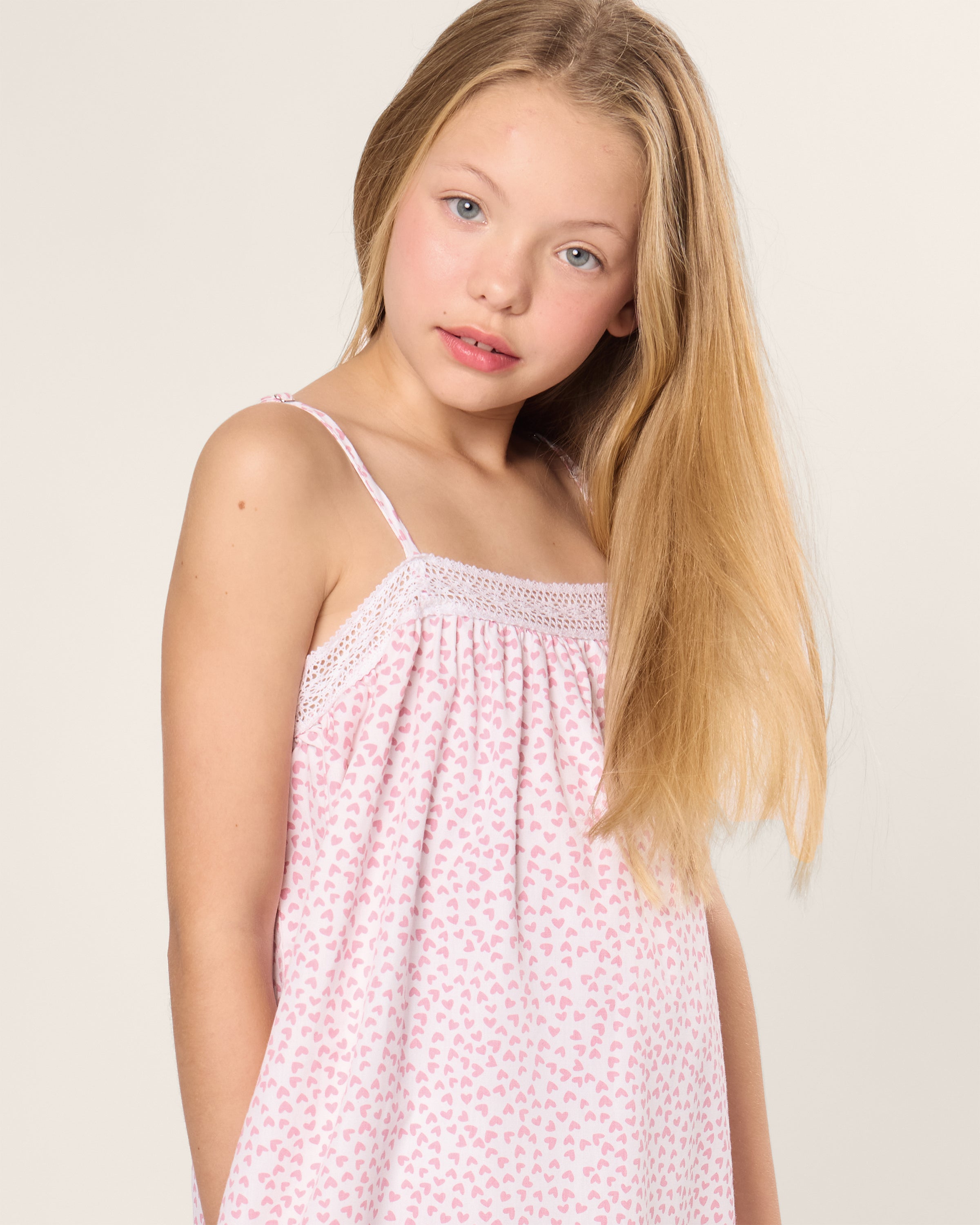 A girl with long blonde hair, wearing Petite Plumes Girls Twill Lily Nightgown in Sweethearts, stands against a plain background.