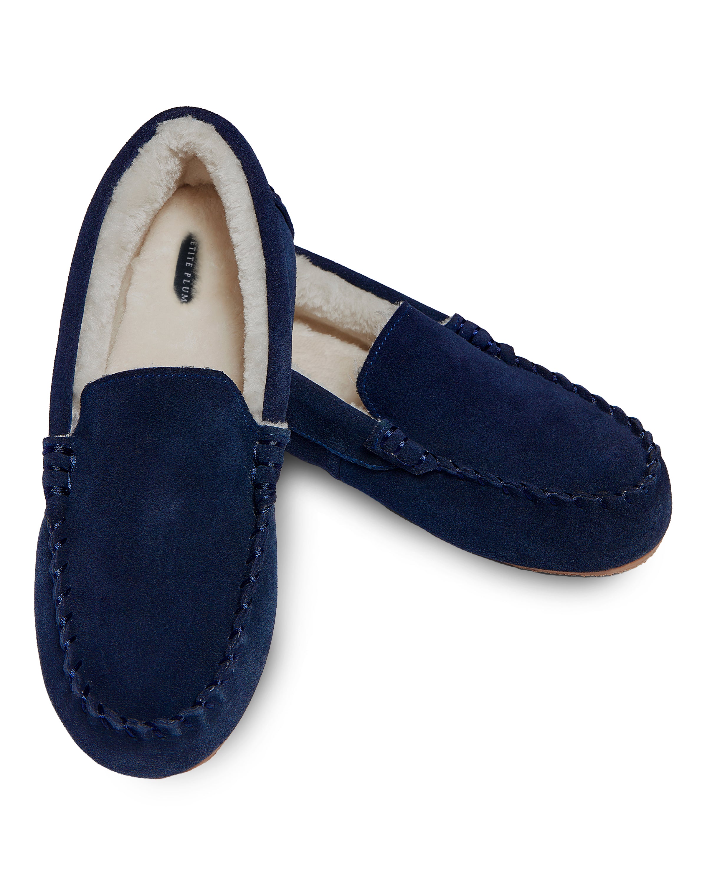 A pair of Petite Plumes Womens Suede Slippers in Navy, featuring ultra-soft faux fur lining, is shown with one slipper slightly in front of the other on a white background.