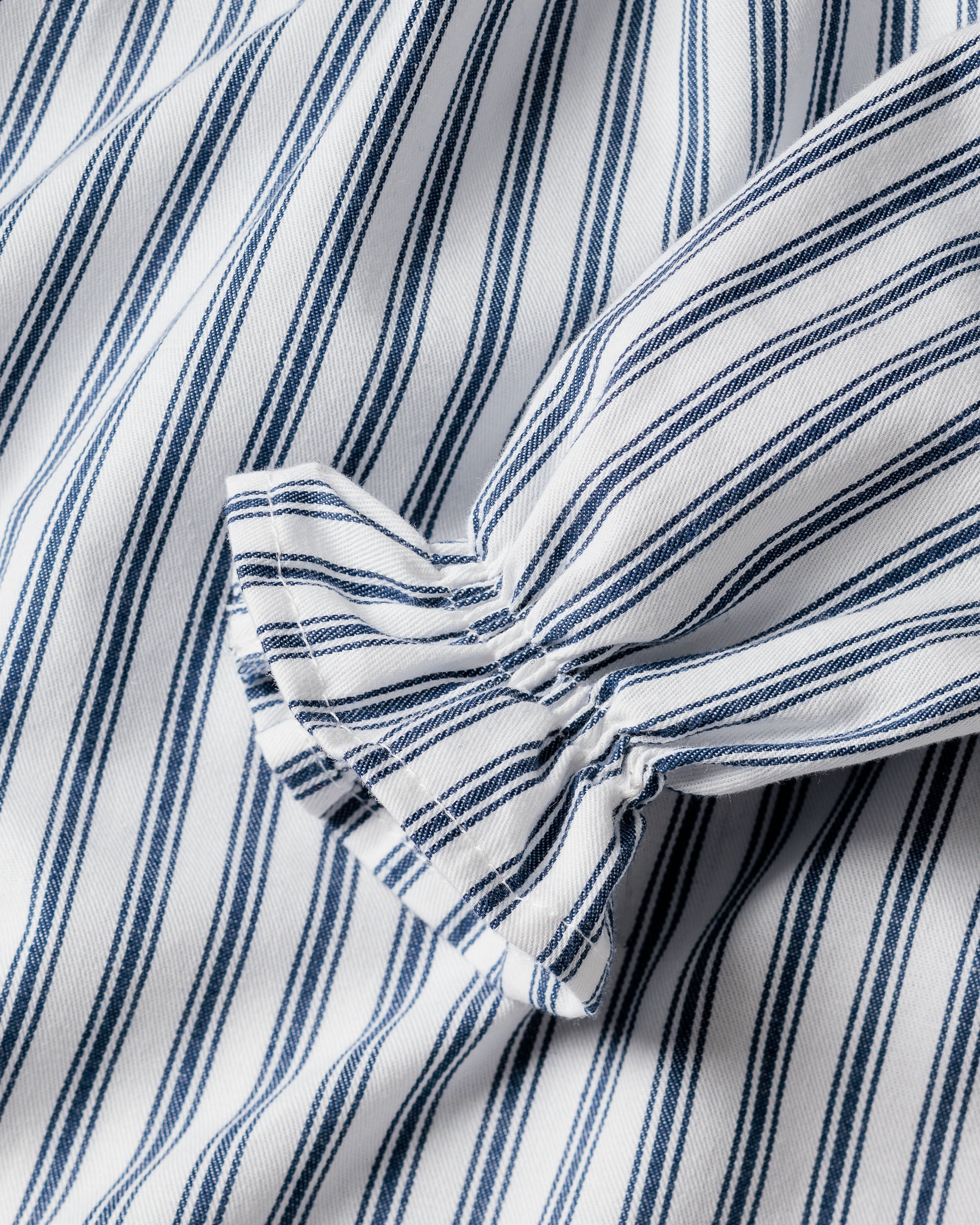 The Girls Twill Delphine Nightgown in Navy French Ticking by Petite Plume showcases flame-retardant fabric with blue and white vertical stripes. The materials gathered folds create texture, making it ideal for childrens sleepwear while the evenly spaced stripes enhance visual rhythm.