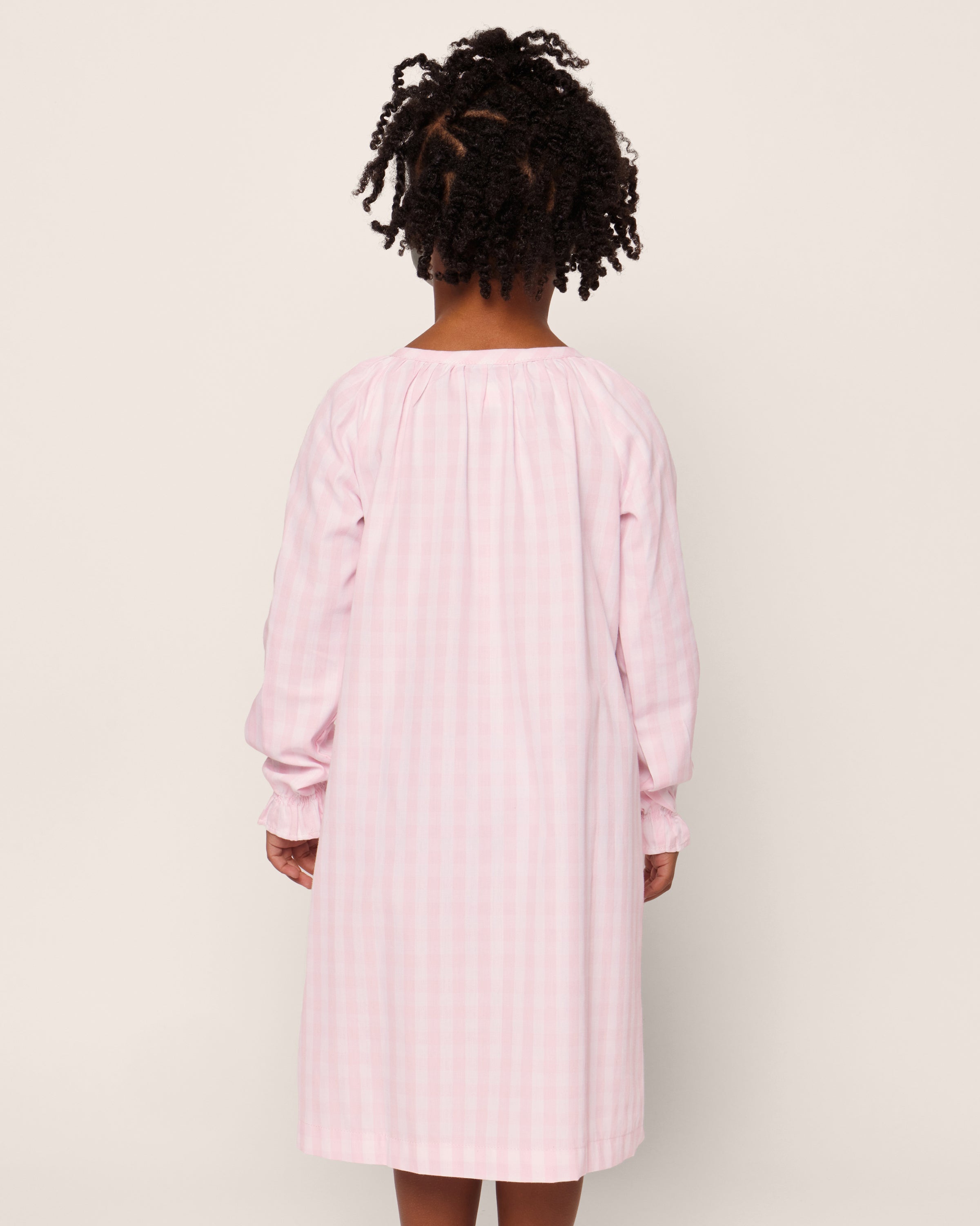 The Petite Plume Girls Twill Delphine Nightgown in Pink Gingham features long sleeves, a rounded neckline with a small keyhole opening, and ruffled cuffs, made from flame-retardant fabric.