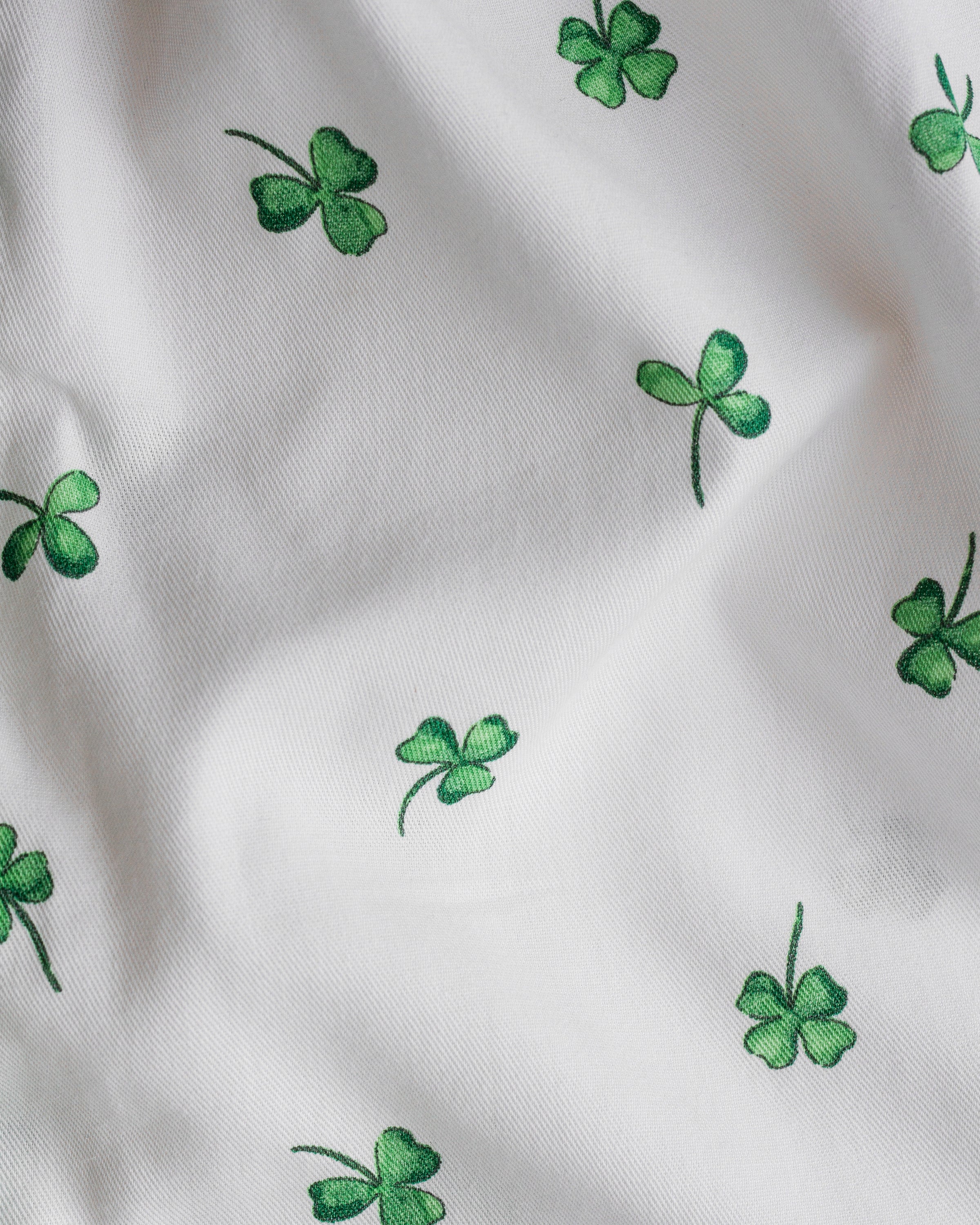 The Girls Twill Delphine Nightgown in Shamrocks by Petite Plume features a lively white fabric with green four-leaf clovers of varying sizes and orientations, perfect for creating luxurious and festive sleepwear.