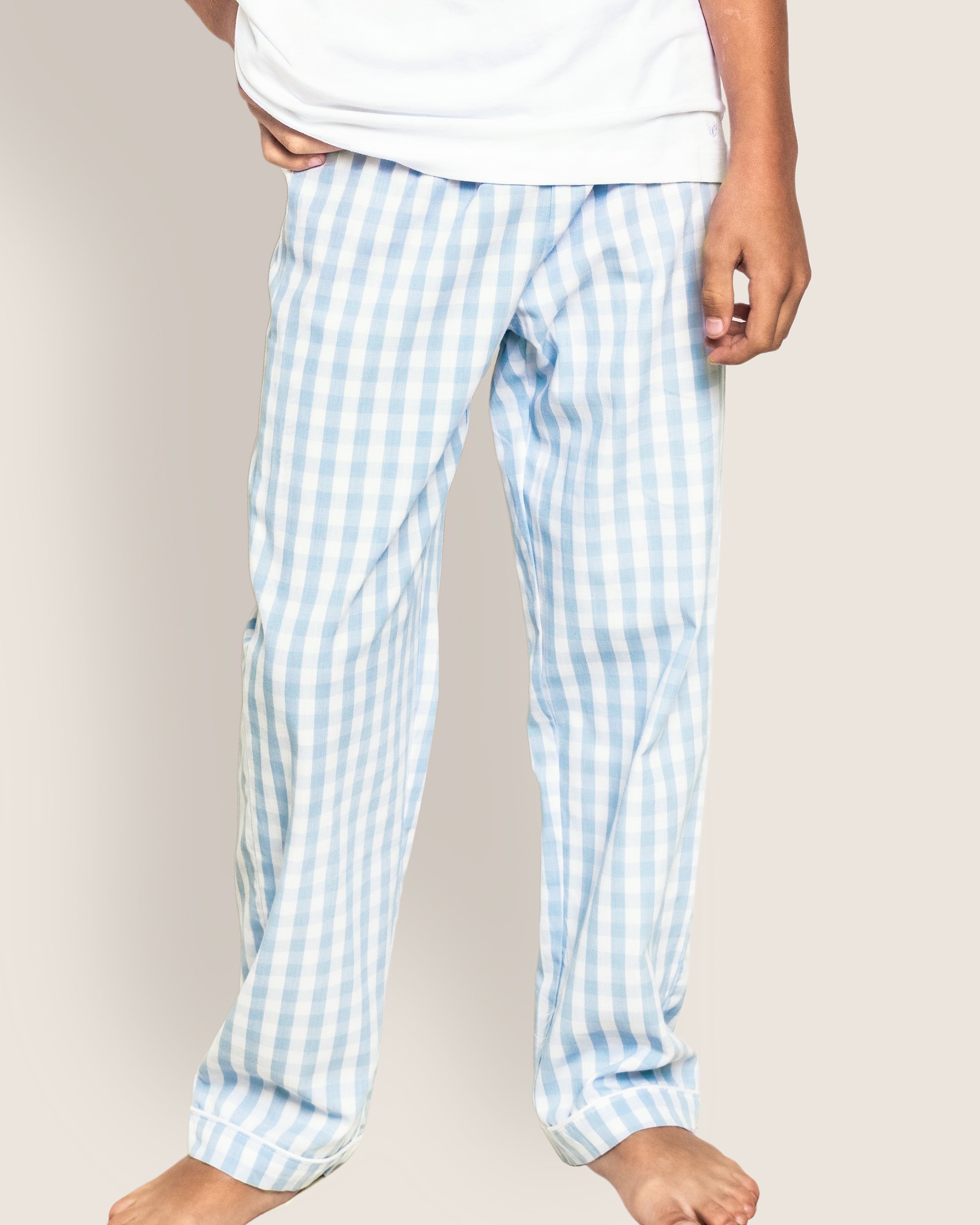 A person stands barefoot in luxurious Petite Plume Kids Twill Pajama Pants in Light Blue Gingham and a white shirt. Crafted from yarn-dyed cotton, their outfit exudes comfort against a neutral background.