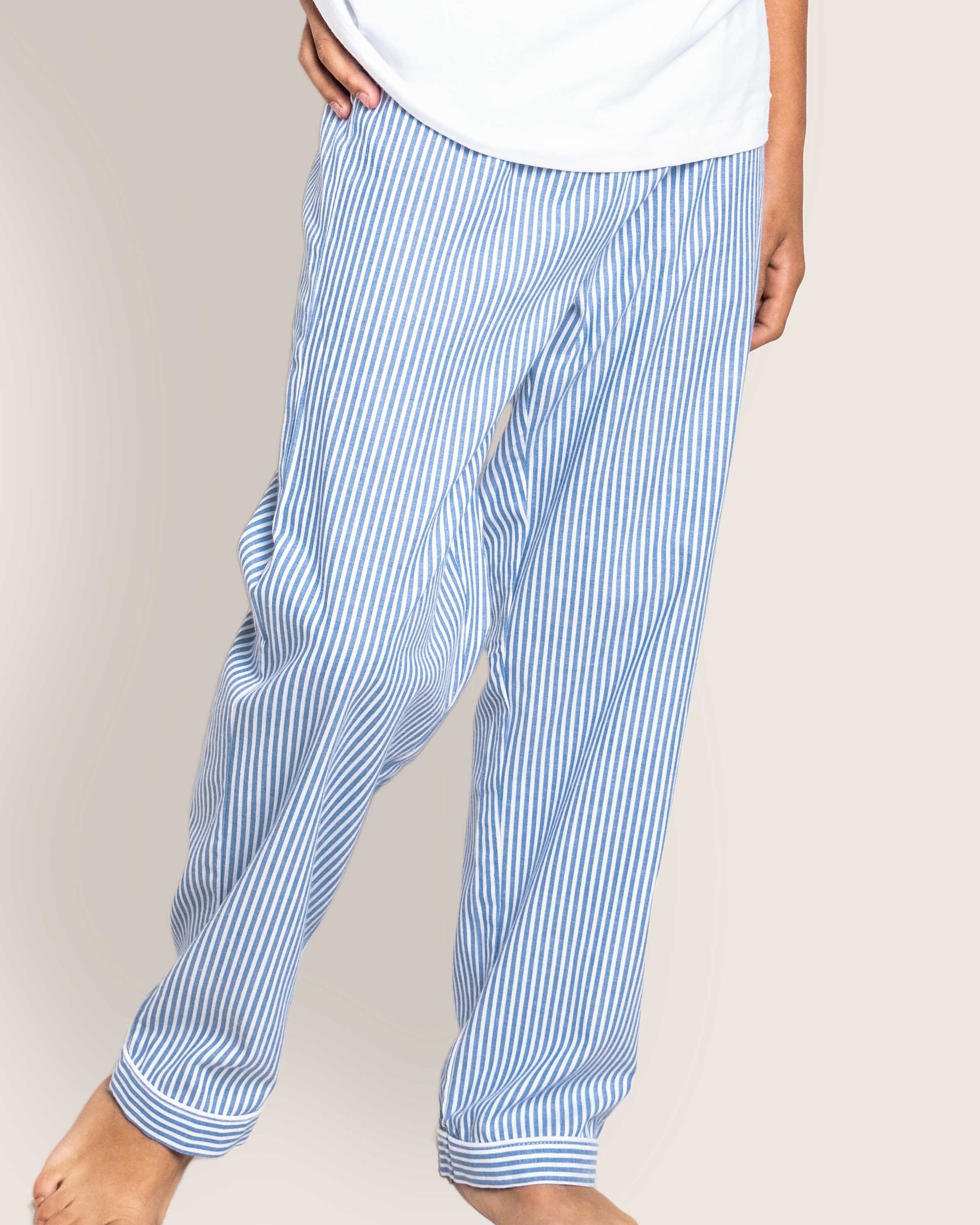 A person stands barefoot against a plain background wearing Petite Plumes Kids Twill Pajama Pants in French Blue Seersucker with a white top.