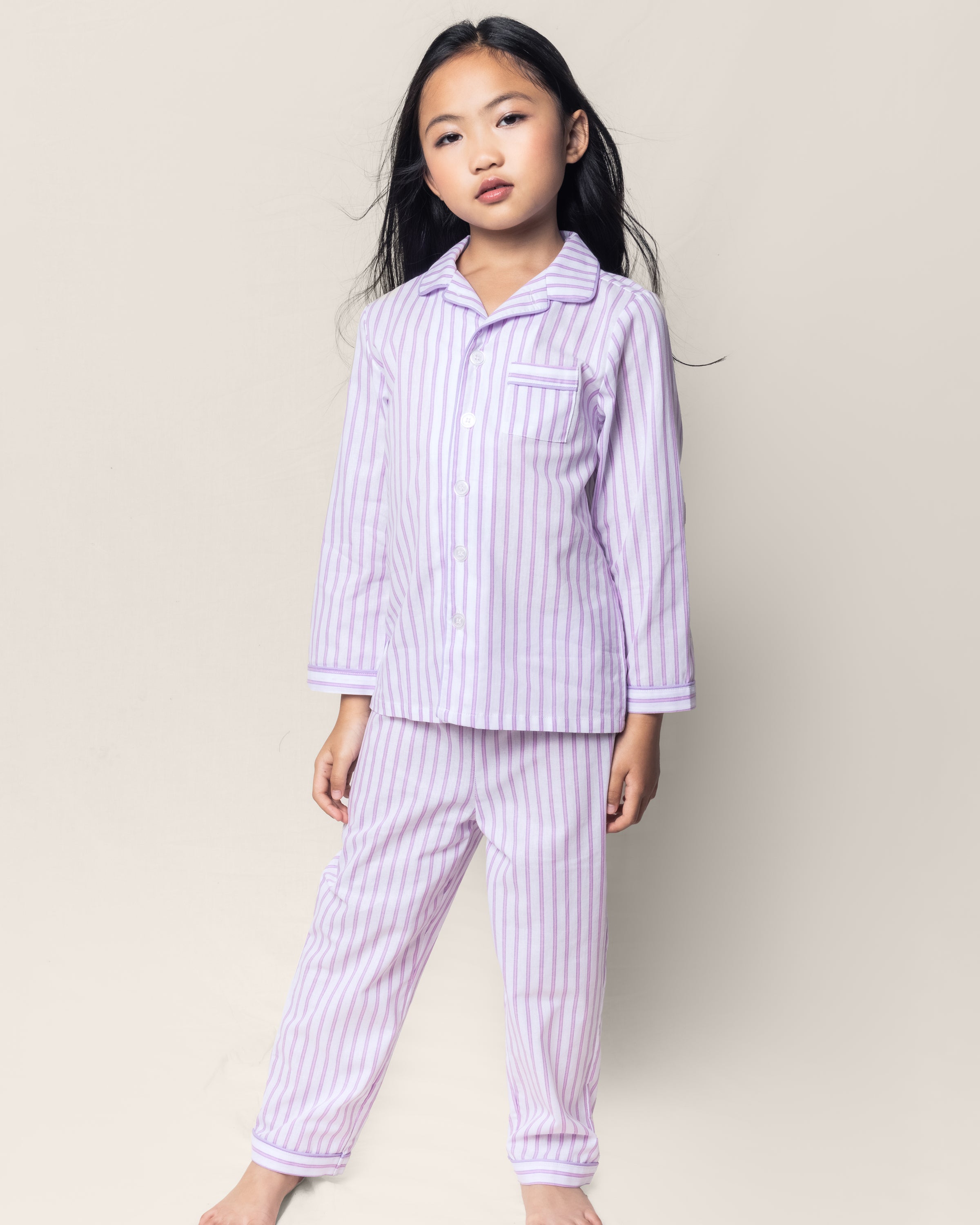 A young girl models the Petite Plume Kids Twill Pajama Set in Lavender French Ticking, standing barefoot with a neutral expression against a simple background.