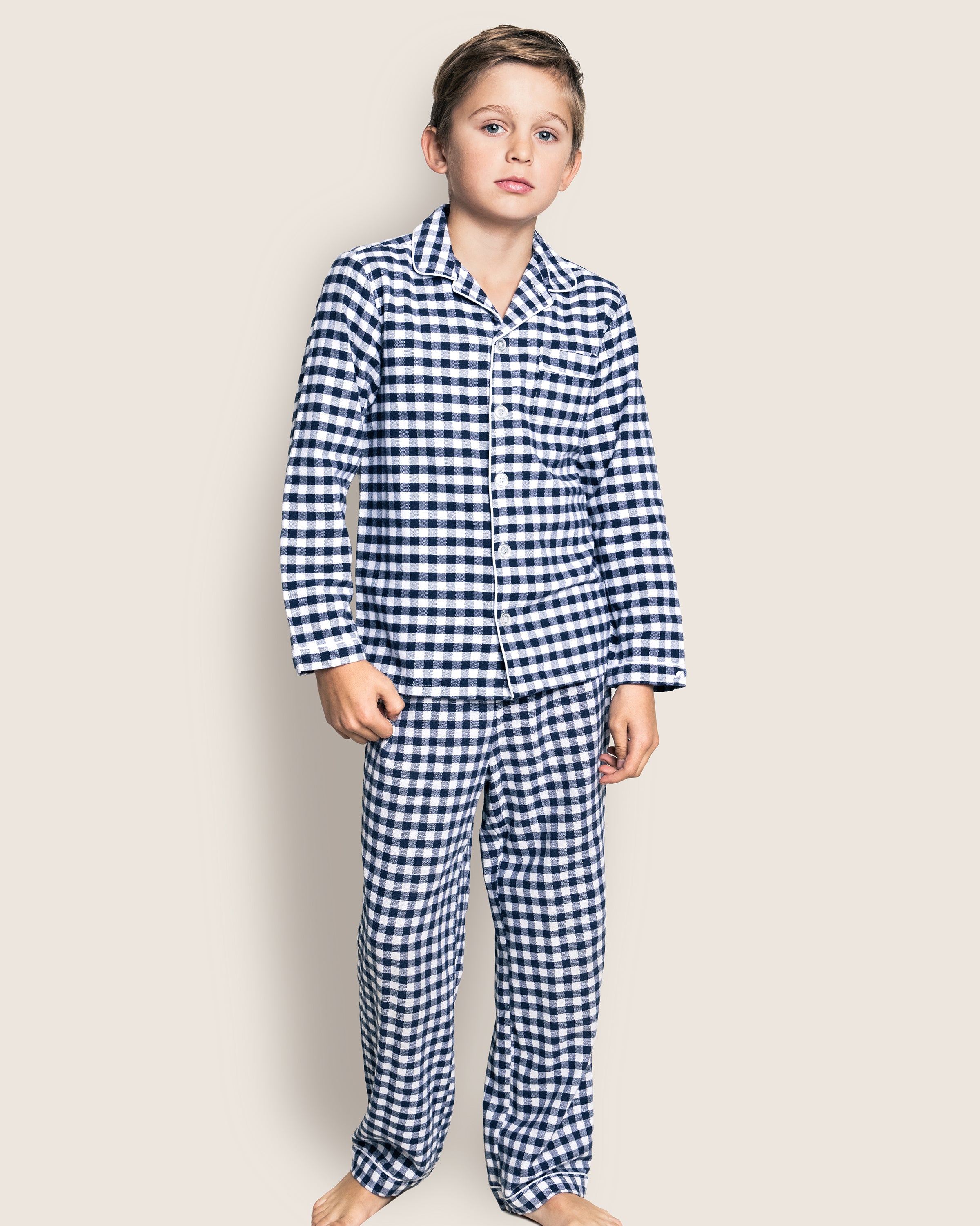 A child is barefoot against a plain background, wearing a Petite Plume Kids Twill Pajama Set in Navy Gingham.