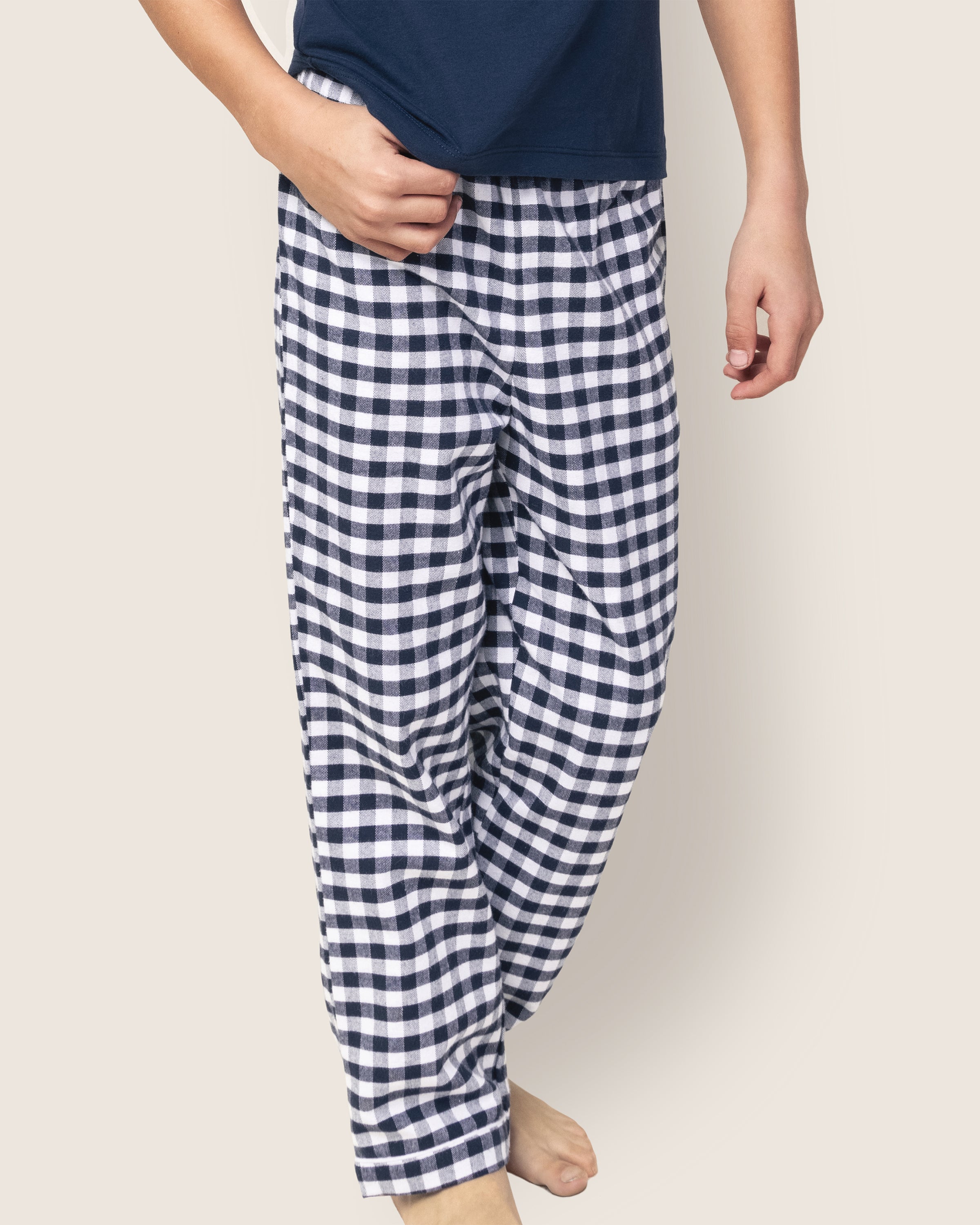 A person in luxurious sleepwear, featuring a navy blue top and Petite Plumes Kids Twill Pajama Pants in Navy Gingham, stands barefoot against a light background.