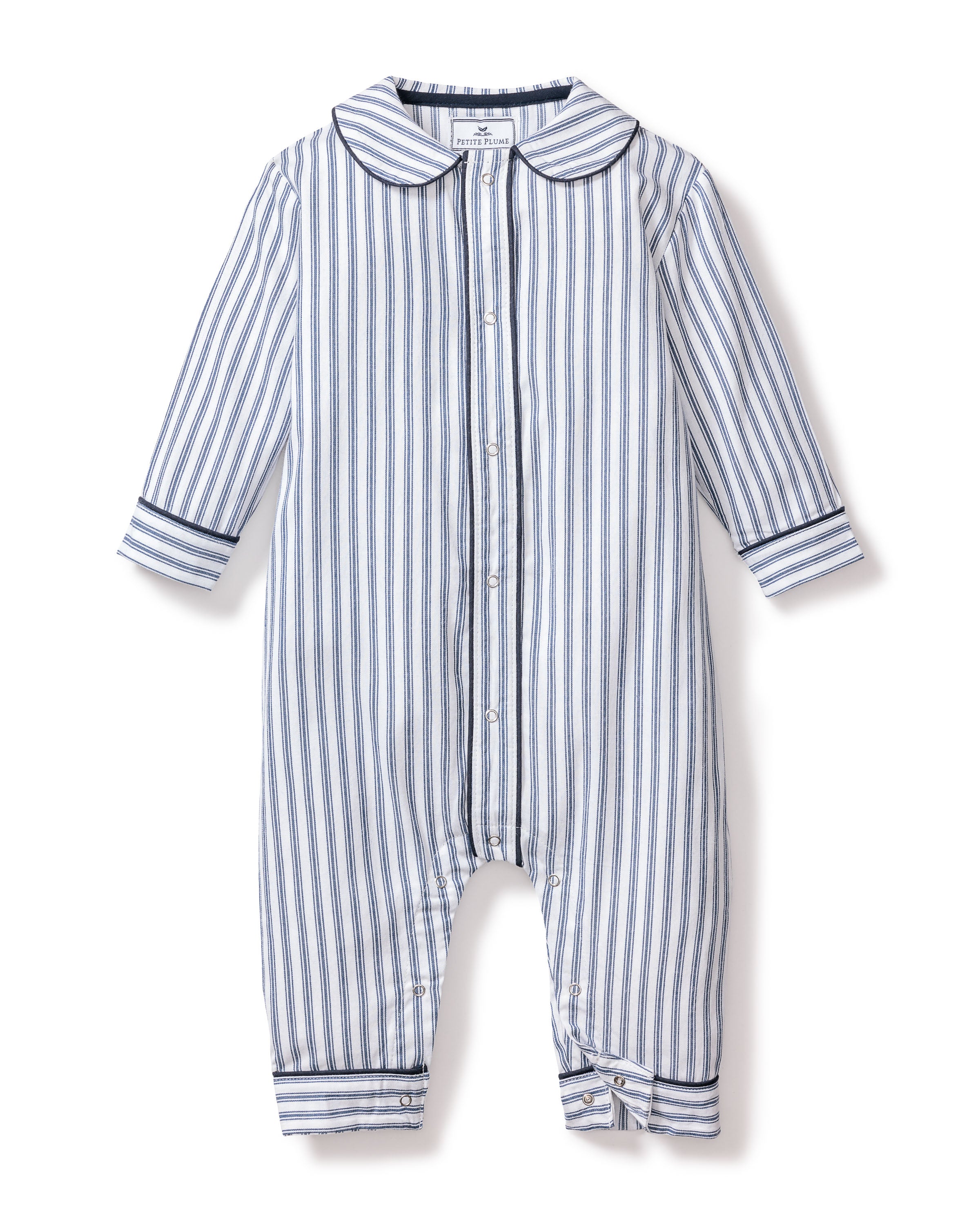 The Babys Twill Cambridge Romper by Petite Plume is crafted from soft brushed twill, perfect for sleepwear. It features long sleeves, a collar, and vertical navy stripes. Front buttons add style, while solid blue bands at the cuffs ensure cozy elegance for your little one.