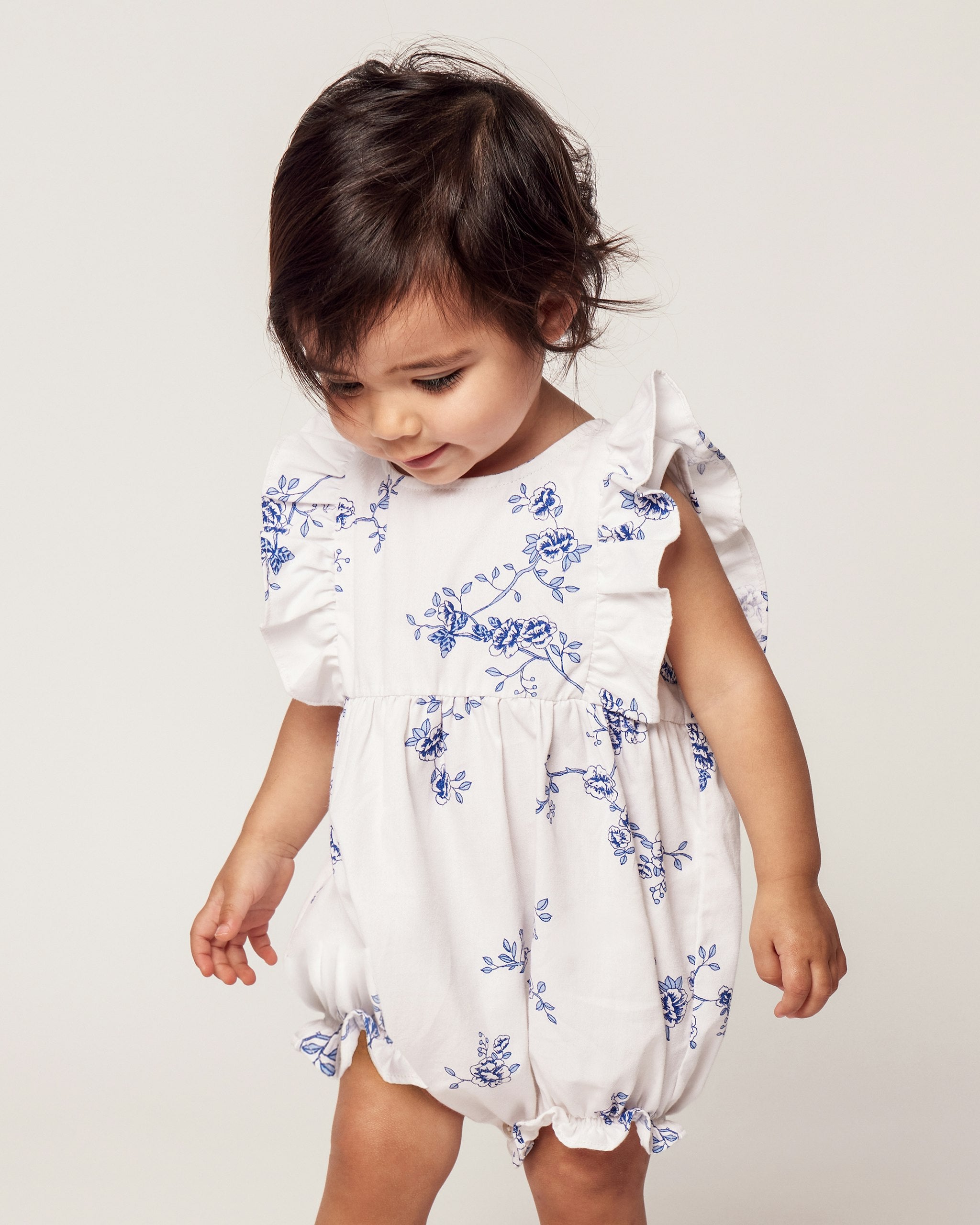 Baby wearing a floral romper on a plain background