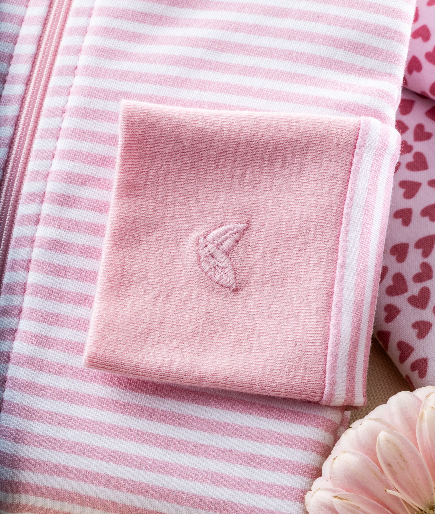 Close-up of Petite Plumes Babys Pima Ruffle Collar Romper in Pink Stripes, showcasing a banana embroidery amidst heart patterns. A soft pink flower peeks from the bottom corner.