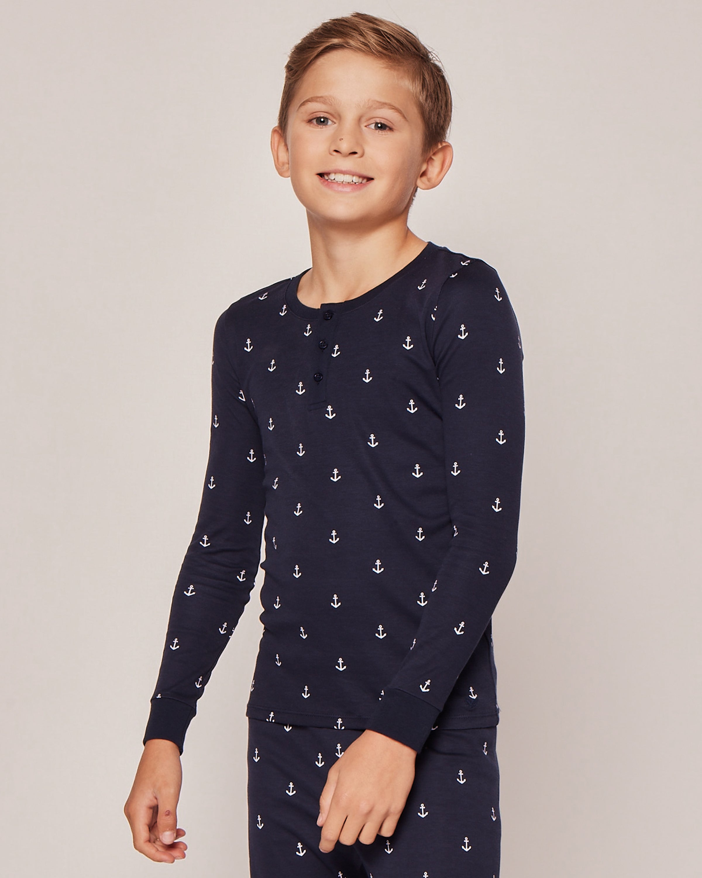 A smiling boy models the Kids Pima Snug Fit Pajama Set in Portsmouth Anchors by Petite Plume, showcasing ultimate sleepwear comfort against a plain backdrop.