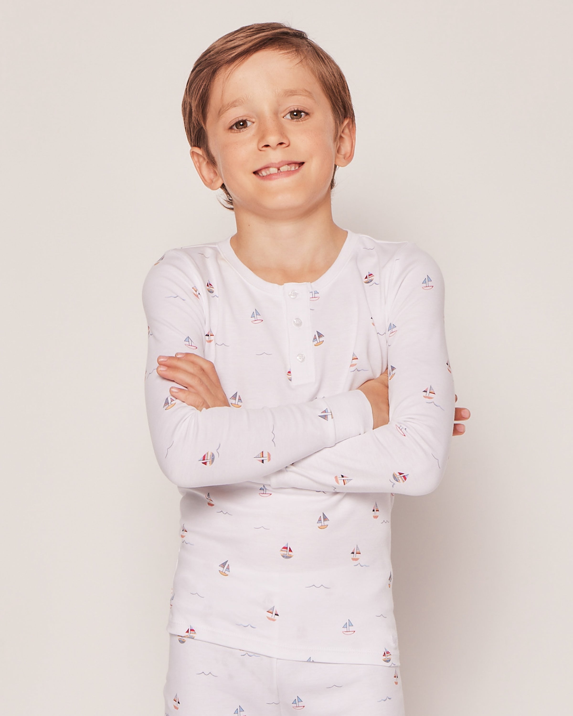 Boy smiling with arms crossed, wearing Petite Plumes Kids Pima Snug Fit Pajama Set in Bateau with small sailboat prints.