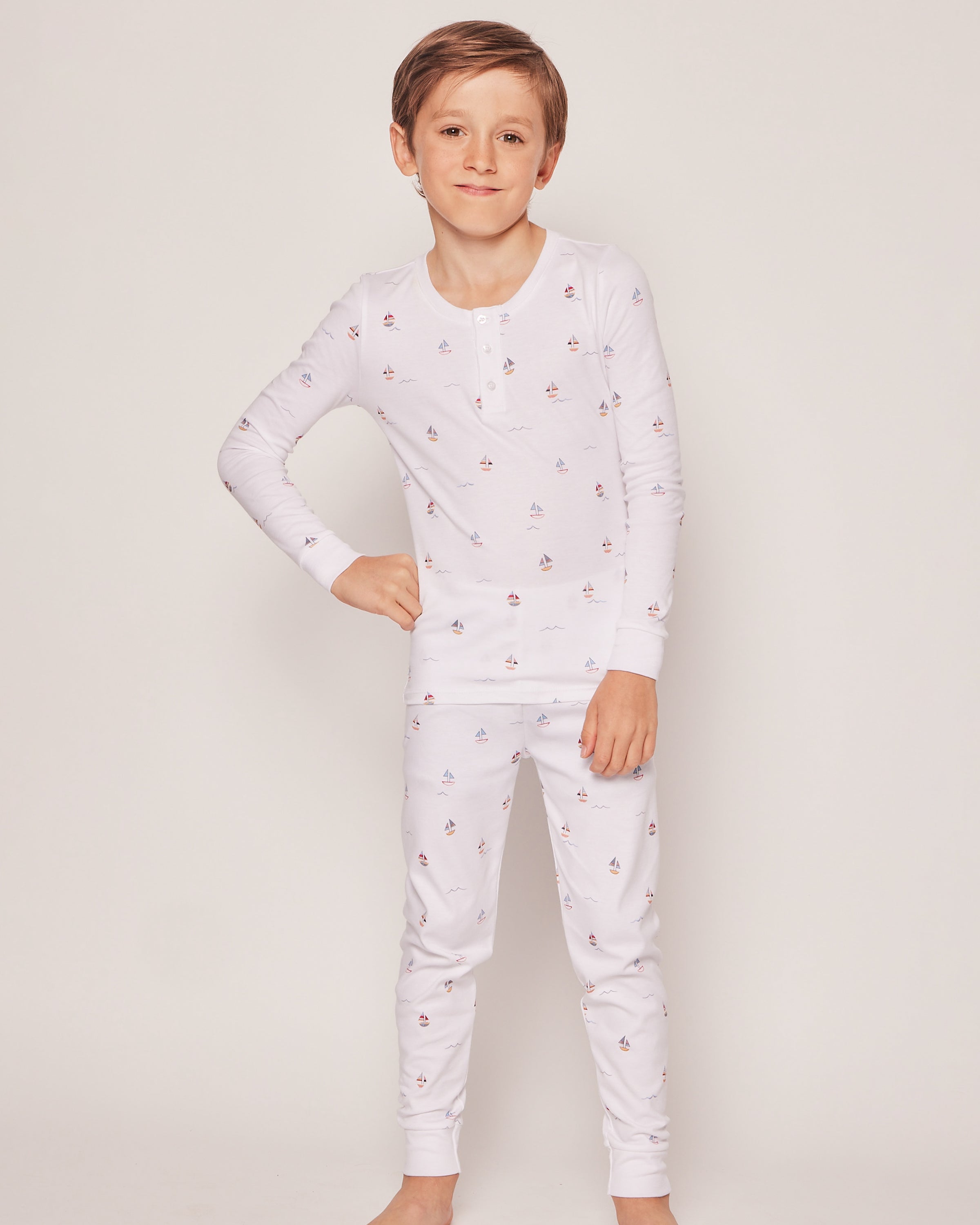 A young boy poses confidently with one hand on his hip, showcasing the charm of his Kids Pima Snug Fit Pajama Set in Bateau by Petite Plume against a plain light background.