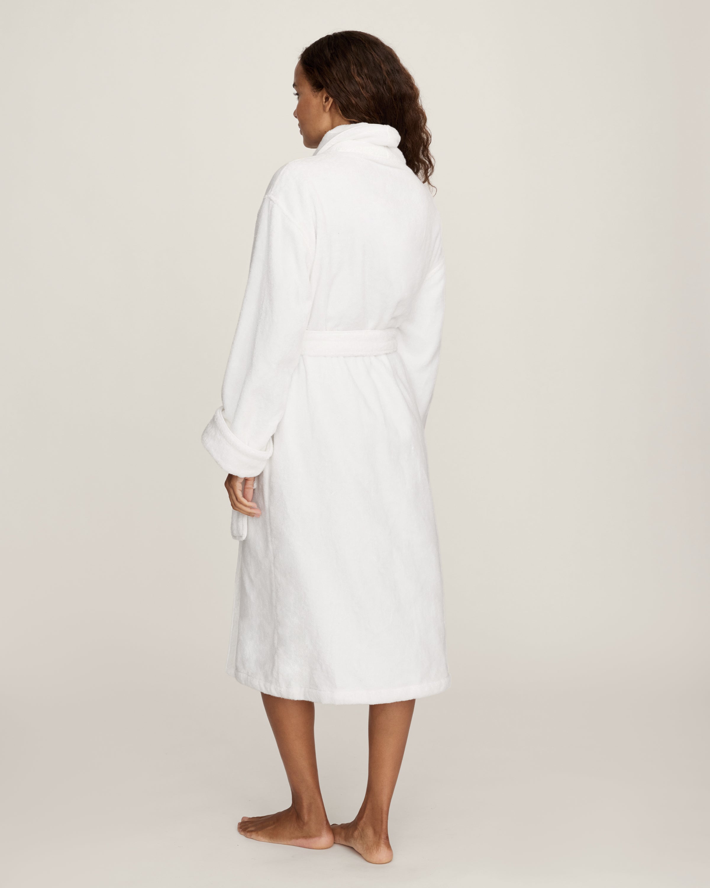 The Unisex Luxe Terry Robe in White features long sleeves, a shawl collar, two front pockets, and a waist tie belt, displayed against a white background.