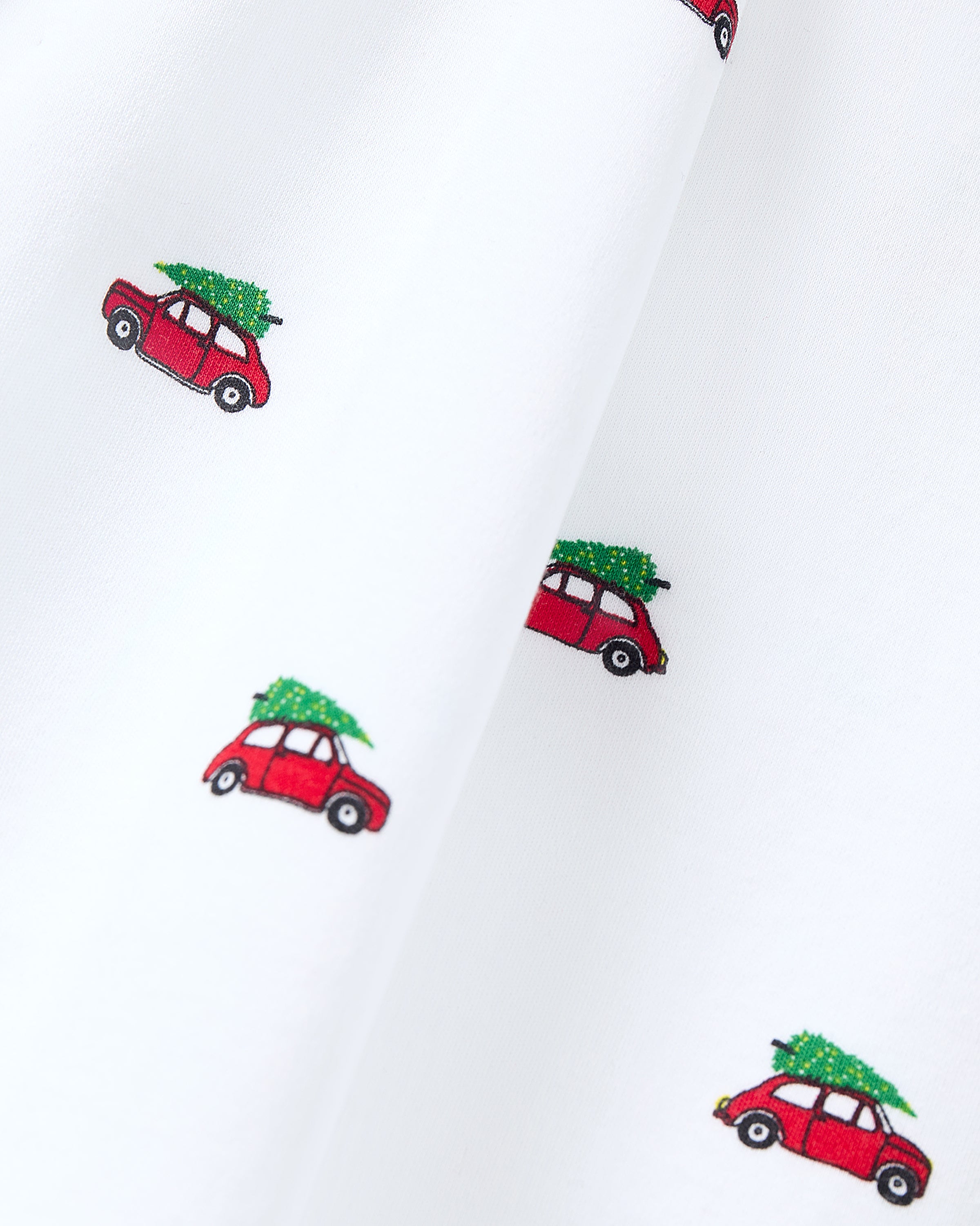 The Petite Plume Pima Baby Blanket in Holiday Journey is a luxury blanket made from soft Pima Cotton. It features white fabric with small red cars, each carrying a green Christmas tree on the roof, arranged evenly and oriented in a single direction for a charming design.