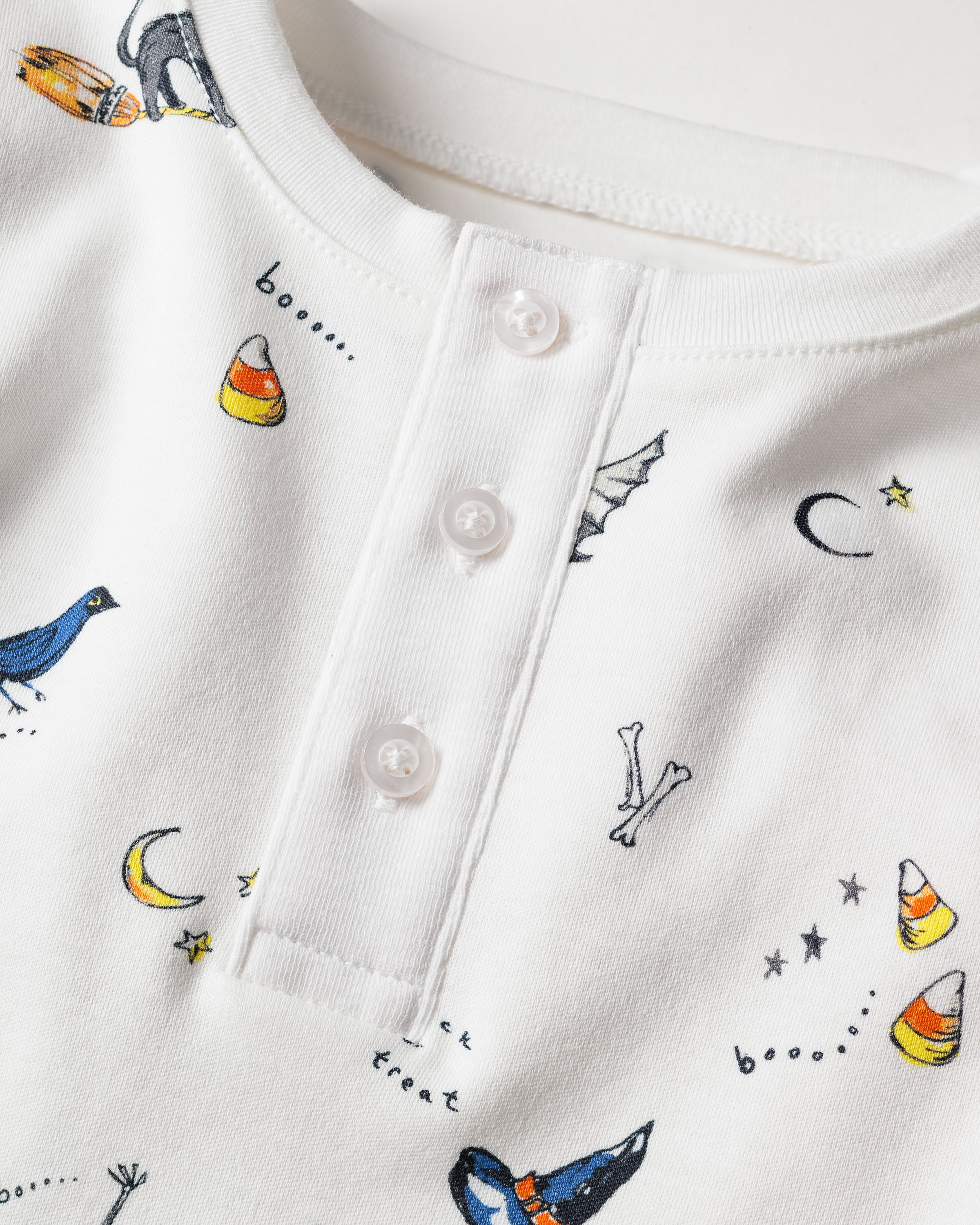 The Kids Pima Snug Fit Pajama Set in Trick or Treat by Petite Plume is a luxurious white sleepwear piece made of soft Pima cotton, featuring Halloween-themed prints such as candy corn, black crow, bats, crescent moons, stars, and fun phrases like trick or treat and boo...