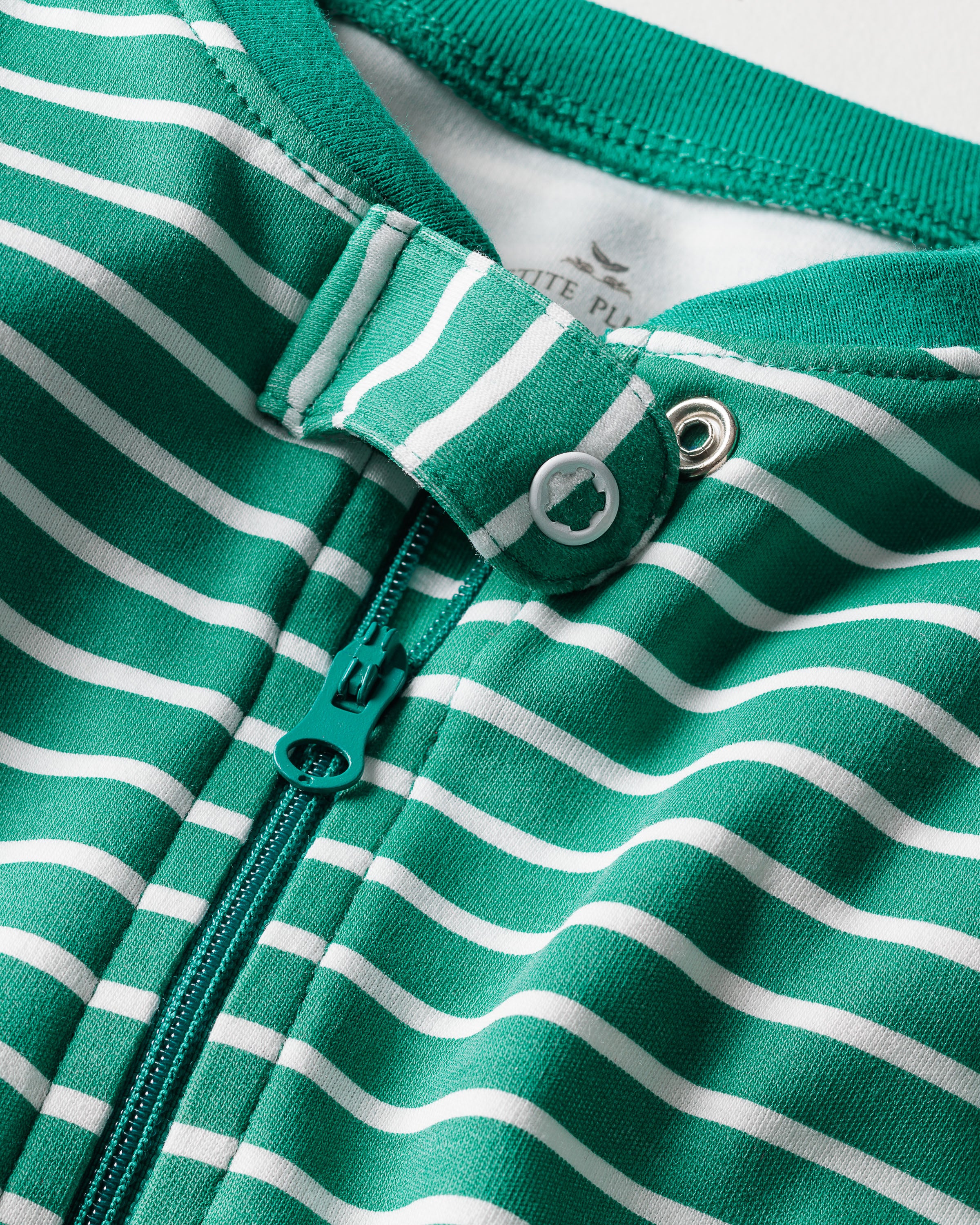 Close-up of Petite Plumes Babys Pima Romper in Green Stripe, crafted from soft Peruvian Pima Cotton. It features a green zipper and snap button at the collar. A tiny tree logo is visible on the label, making it ideal for comfortable daywear.