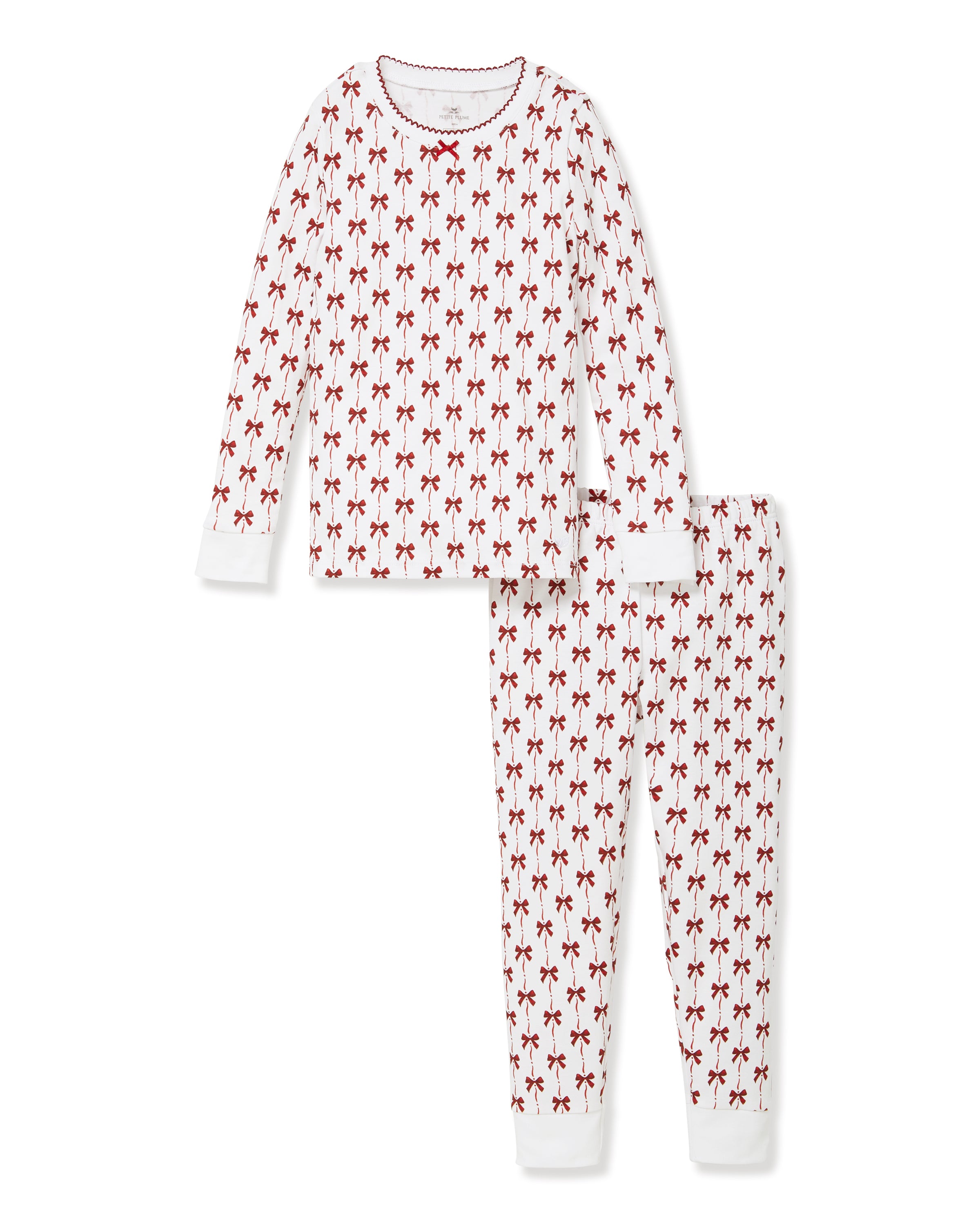 The Kid's Pima Snug Fit Pajama Set in Blissful Bows features a white two-piece design with long sleeves and pants, decorated with a repeating small red bow pattern and finished with white cuffs on the sleeves and pant legs.