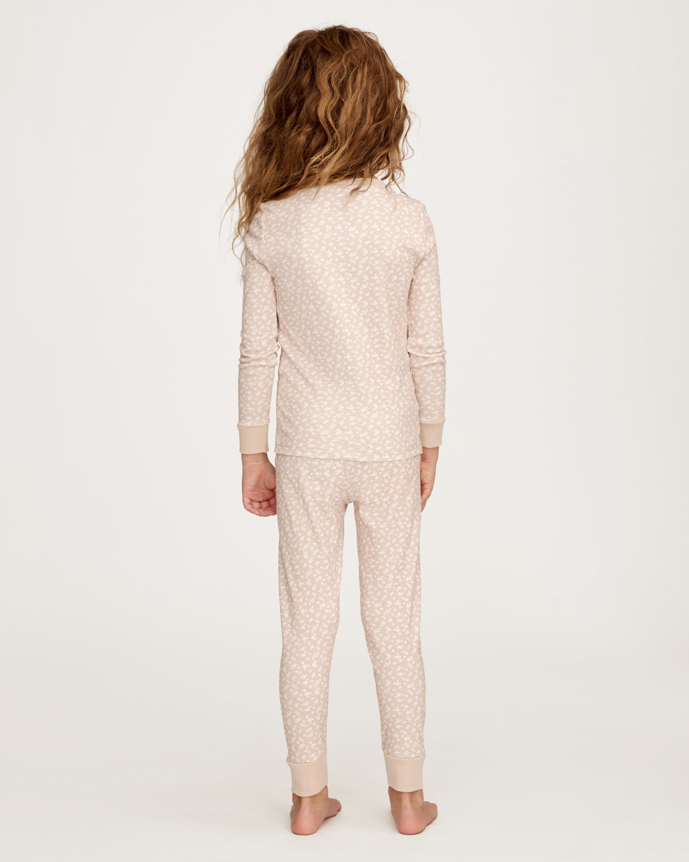 The Kid's Pima Snug Fit Pajama Set in Ditsy Waltz Camel features a beige long-sleeve top and matching pants with a white floral pattern and solid beige cuffs on the sleeves, neckline, and pant legs.