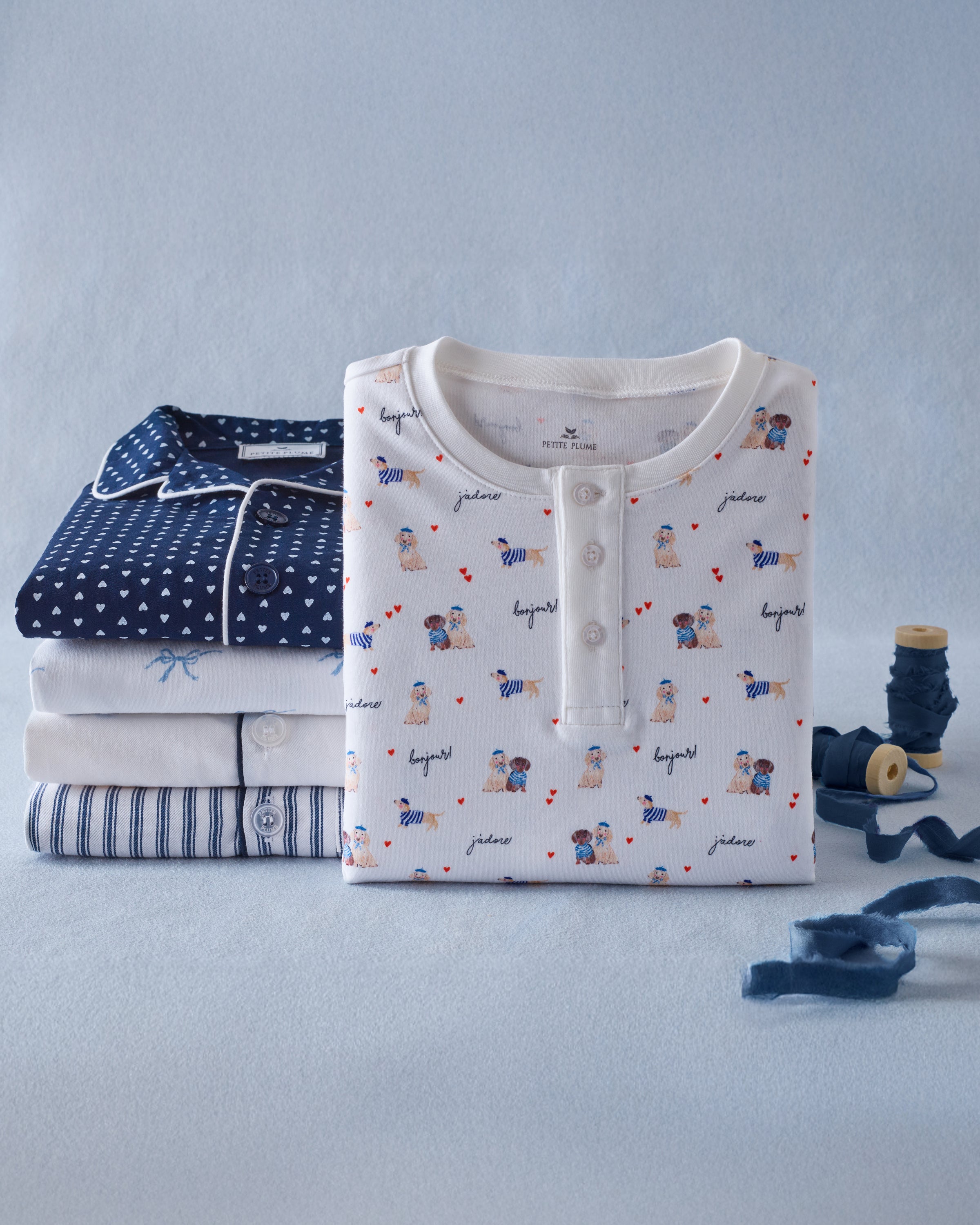 The Kid's Pima Snug Fit Pajama Set in Le Woof is a white long-sleeve pajama set with matching pants, featuring a colorful all-over cartoon dog and bone print, plus cuffed sleeves and ankles for a snug fit.