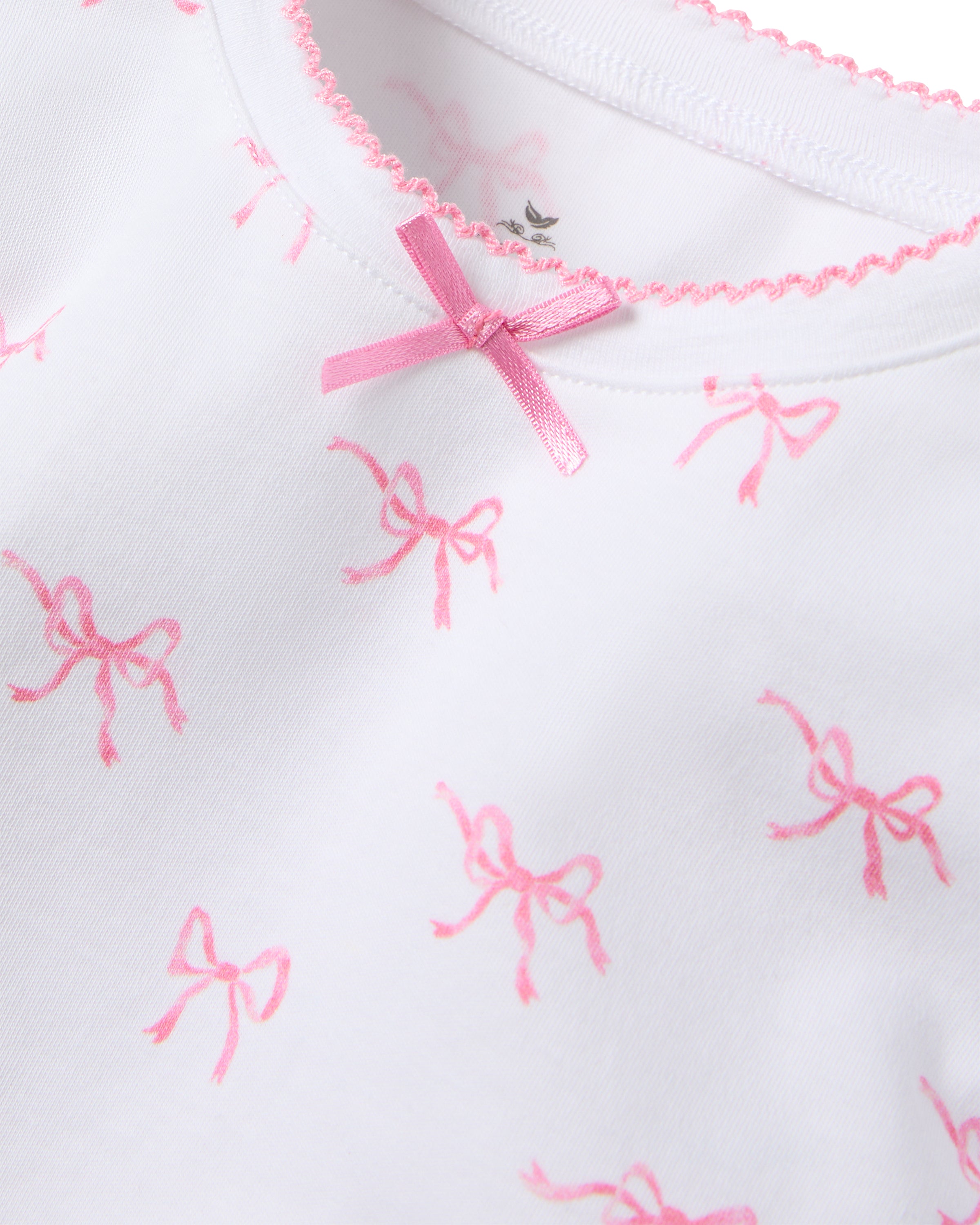 The Kid’s Pima Snug Fit Pajama Set in Blushing Bows by Petite Plume features a white shirt with pink bows, crafted from soft Pima cotton for ultimate comfort and sweet dreams.
