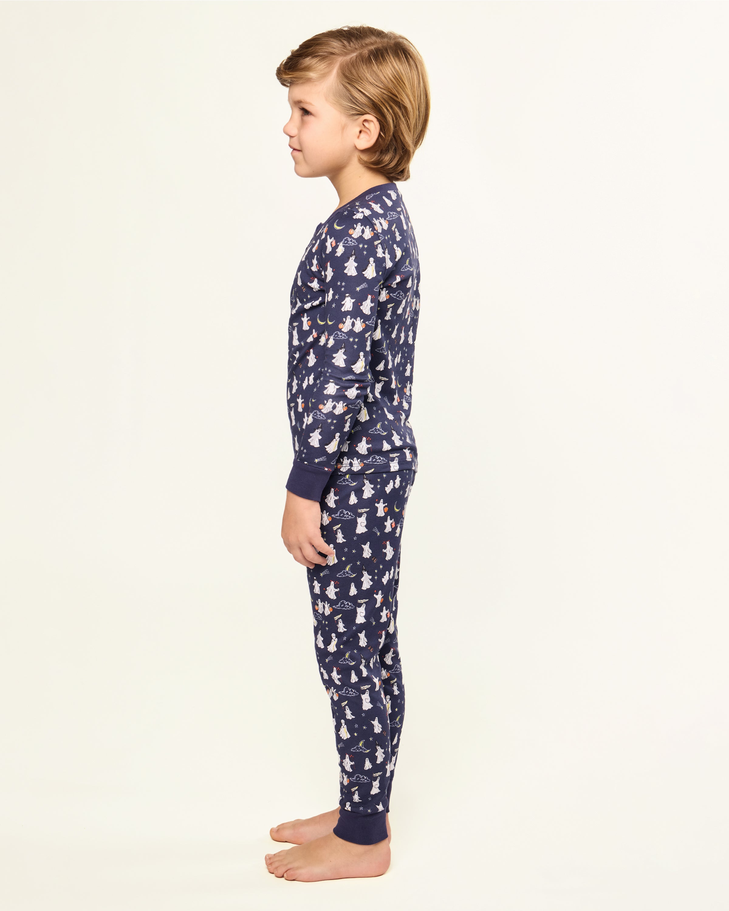 The Kid's Pima Snug Fit Pajama Set in Spooky Slumber is a navy blue pajama set with long sleeves and pants, featuring white and red cartoon dogs in winter gear, plus dark blue cuffs and button details on the top.