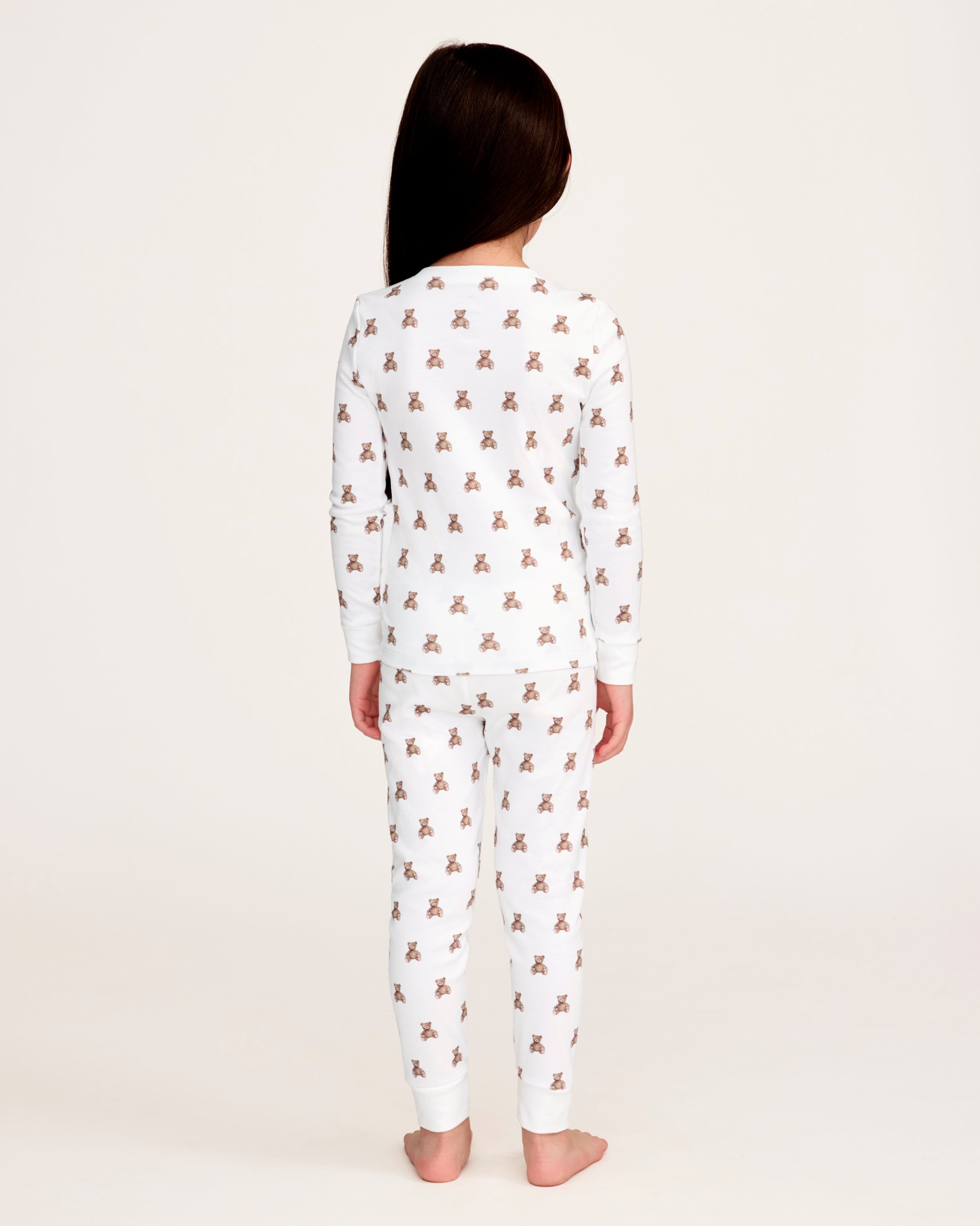 The Kid's Pima Snug Fit Pajama Set in Teddy Tales features a white long-sleeve buttoned top and elastic waist pants with ribbed cuffs, both printed all over with brown teddy bears. Suitable for children.