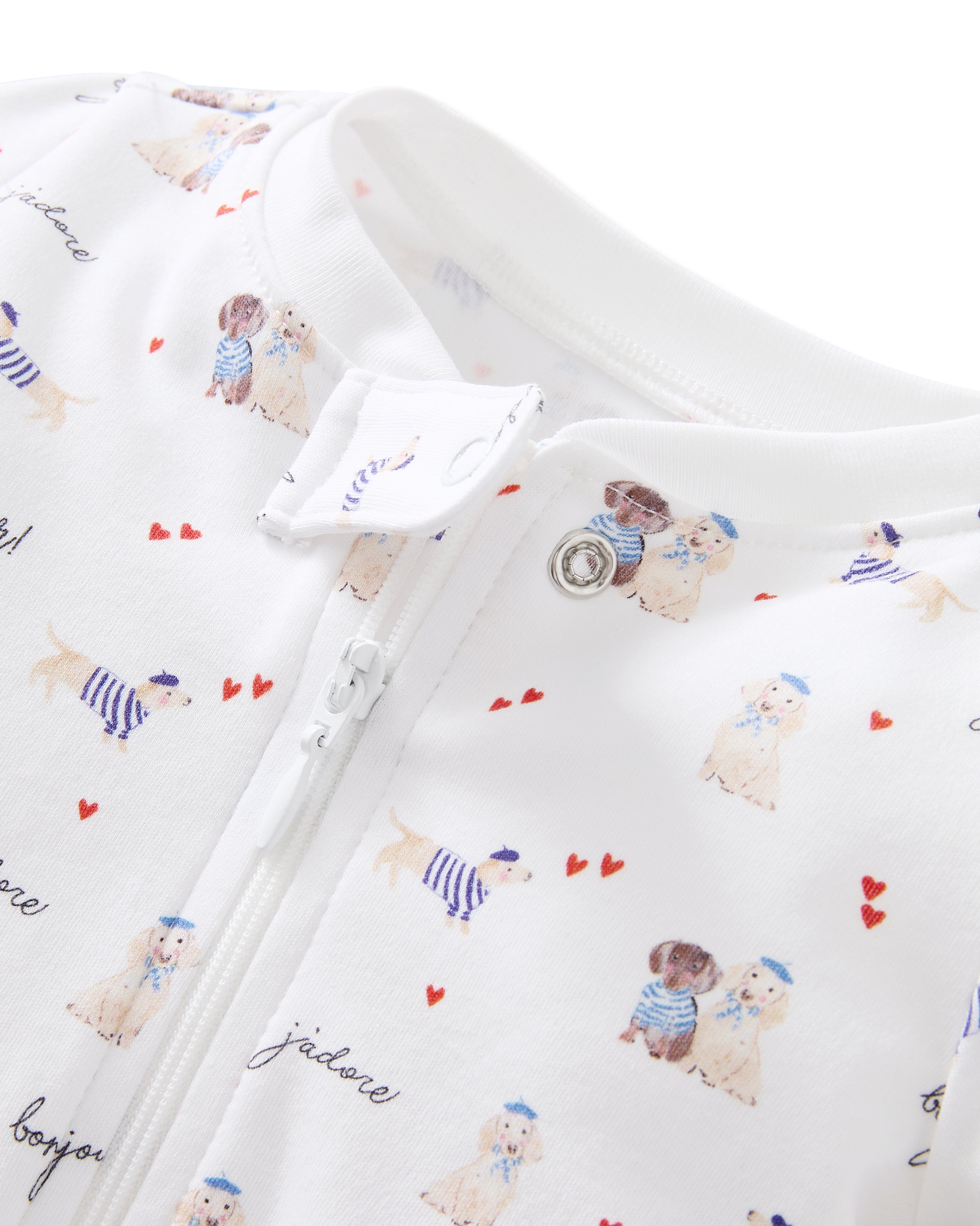 The Baby's Pima Romper in Le Woof is a white footed onesie with a front zipper, featuring playful blue, red, and tan illustrations and cursive words, plus tiny hearts and charming patterns throughout.
