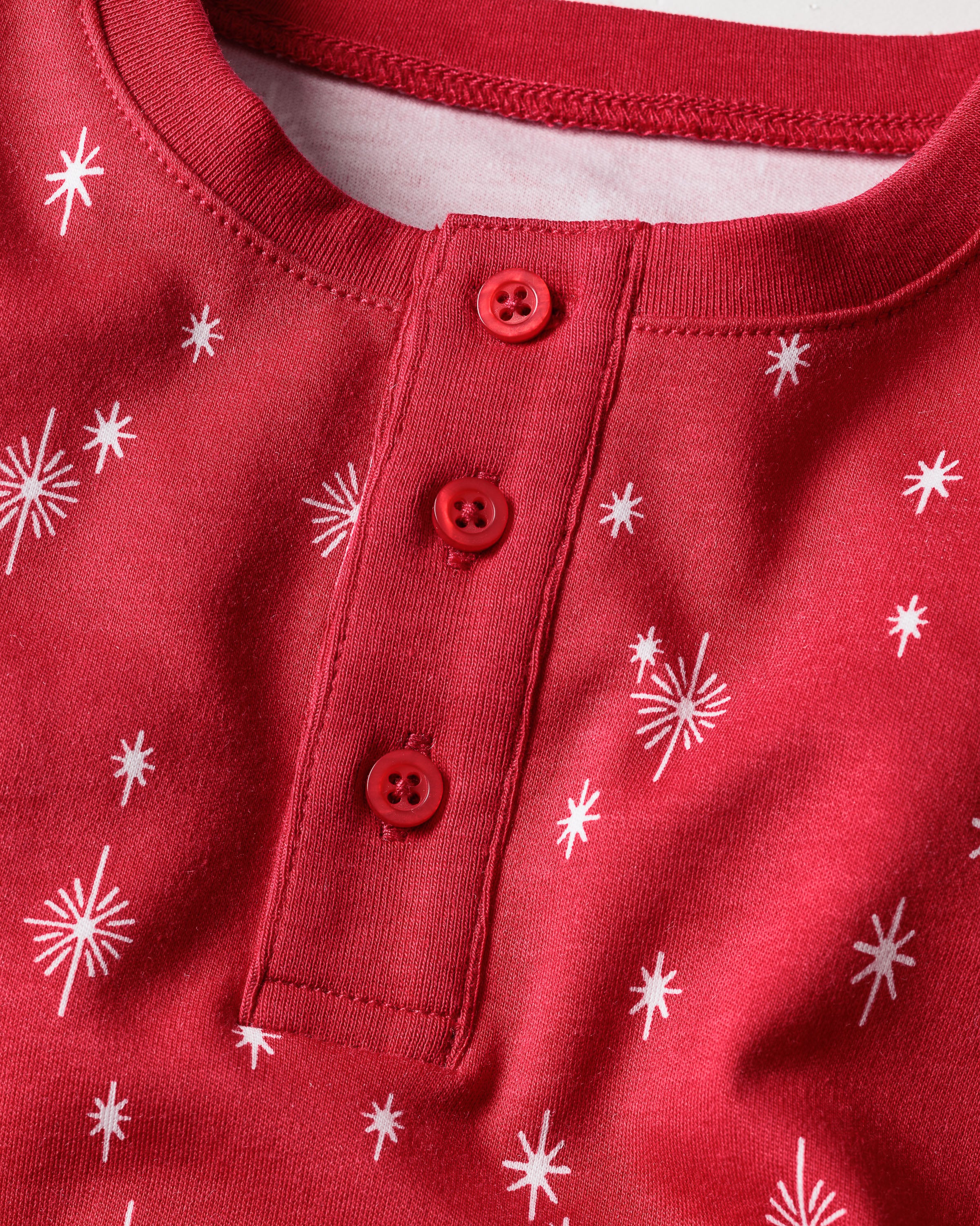 Petite Plumes Kids Pima Snug Fit Pajama Set in Starry Night shows a red top with white snowflakes, featuring long sleeves, a round neckline, and a short placket with three red buttons. Made from soft Pima cotton, it offers cozy comfort for winter sleepwear.