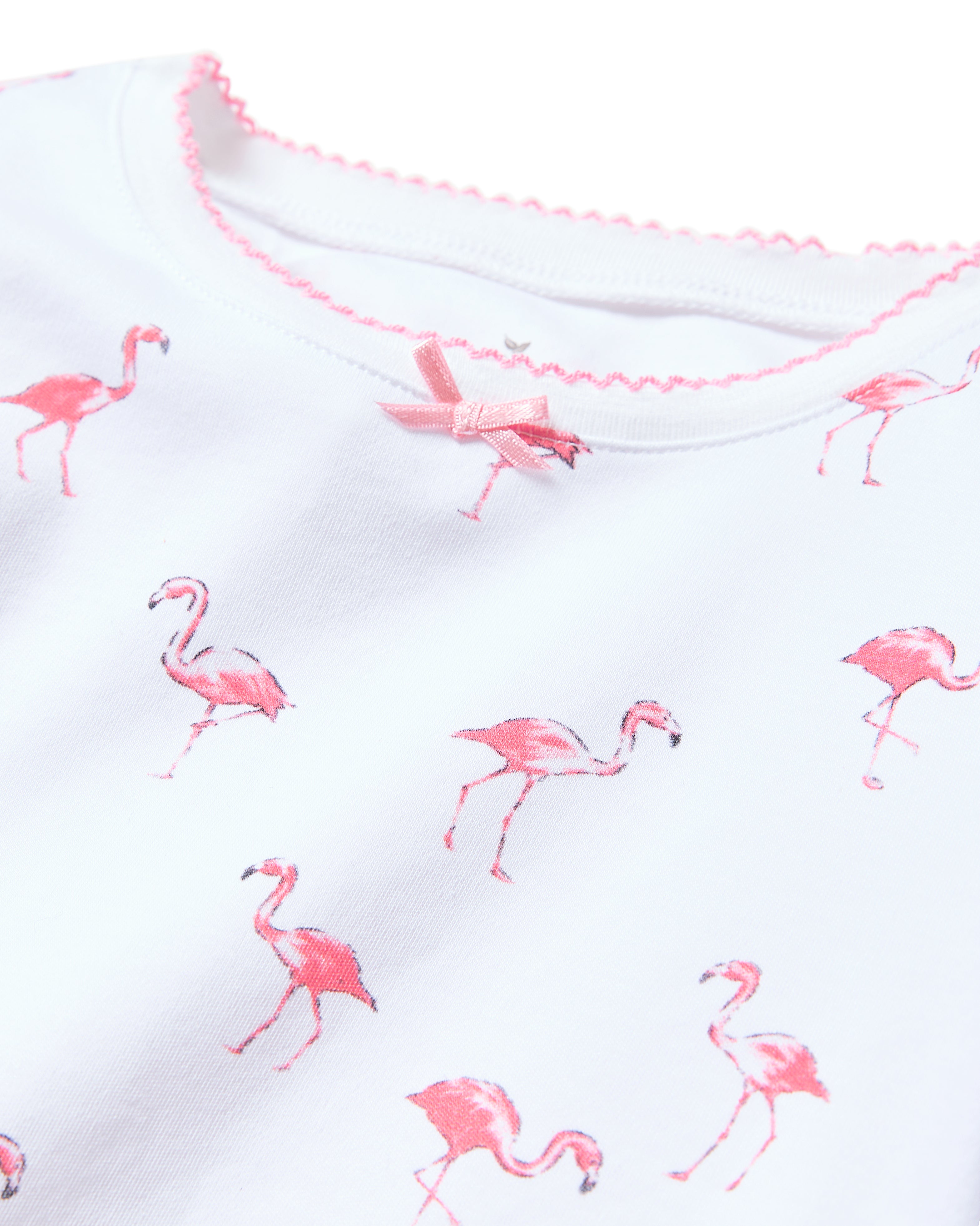 Close-up of Petite Plumes Kids Pima Snug Fit Short Set in Flamingos: a white luxury sleepwear top with pink flamingo print, pink bow at the neckline, and a collar finished with pink scalloped trim.