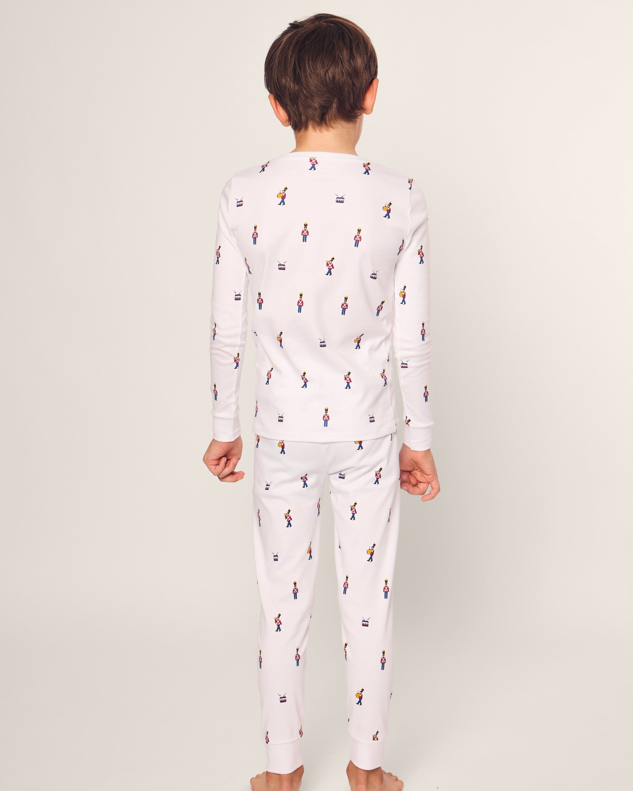 In a light-colored background, a child wears Petite Plumes Kids Pima Snug Fit Pajama Set in Toy Soldier. Crafted from luxurious Pima cotton, the white pajamas feature a vibrant dancer pattern and include a long sleeve top and pants.