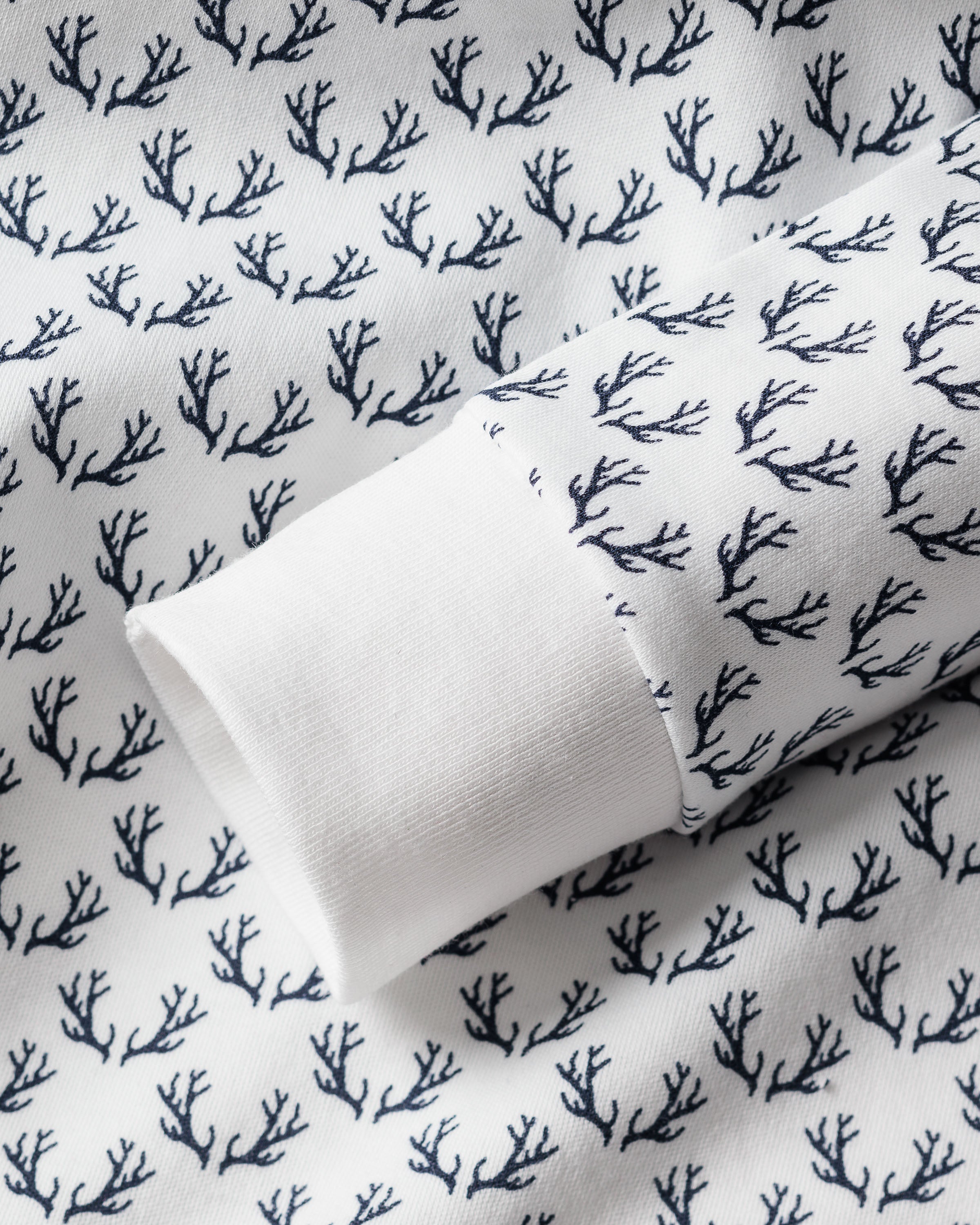 A detailed view of the Kids Pima Snug Fit Pajama Set from Petite Plume showcases a long sleeve top in Nordic Antlers on White, featuring a sophisticated nature-inspired navy blue branch pattern composed of soft Pima cotton.