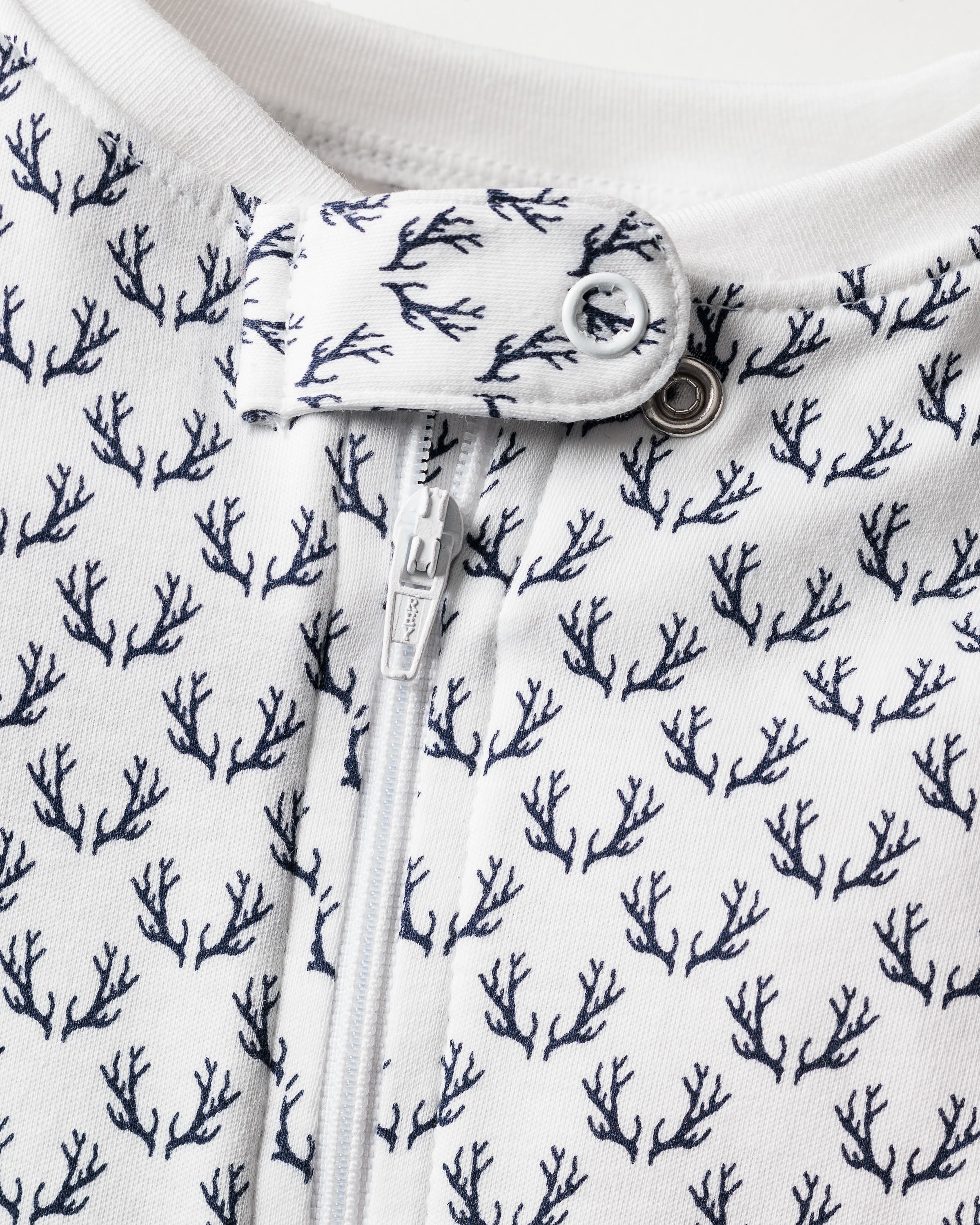 Close-up of Petite Plumes Babys Pima Romper in Nordic Antlers on White, showcasing a dark blue coral pattern. It features a central zipper and snap button closure. The Pima cotton fabric looks soft and textured.