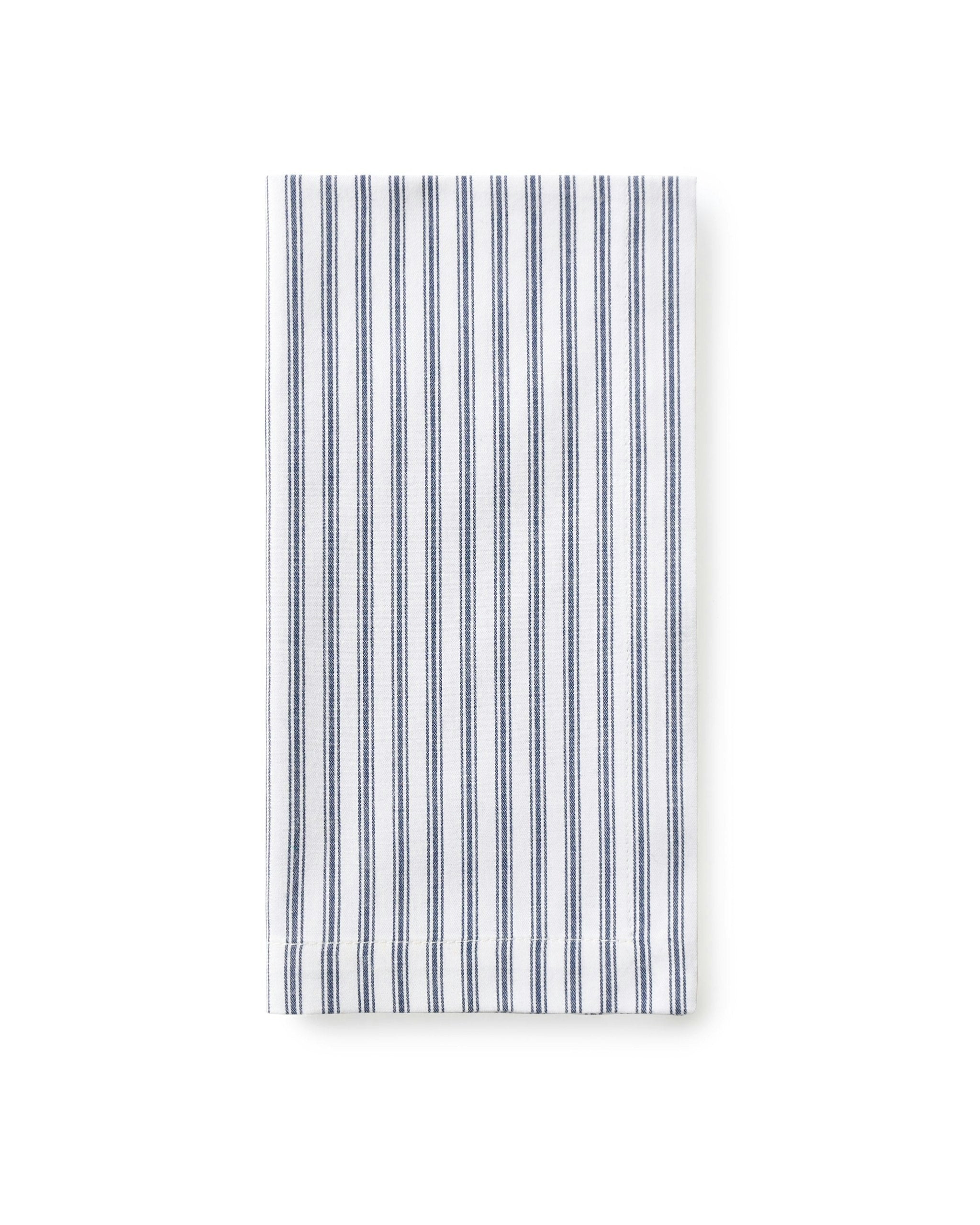 A set table with navy blue and white striped napkins, placed on a plate, with a decorative napkin ring, surrounded by cutlery and a patterned tablecloth in the background.