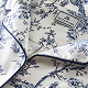 A close-up of white fabric with blue floral patterns and blue piping, featuring a visible label sewn inside with text and a small logo.