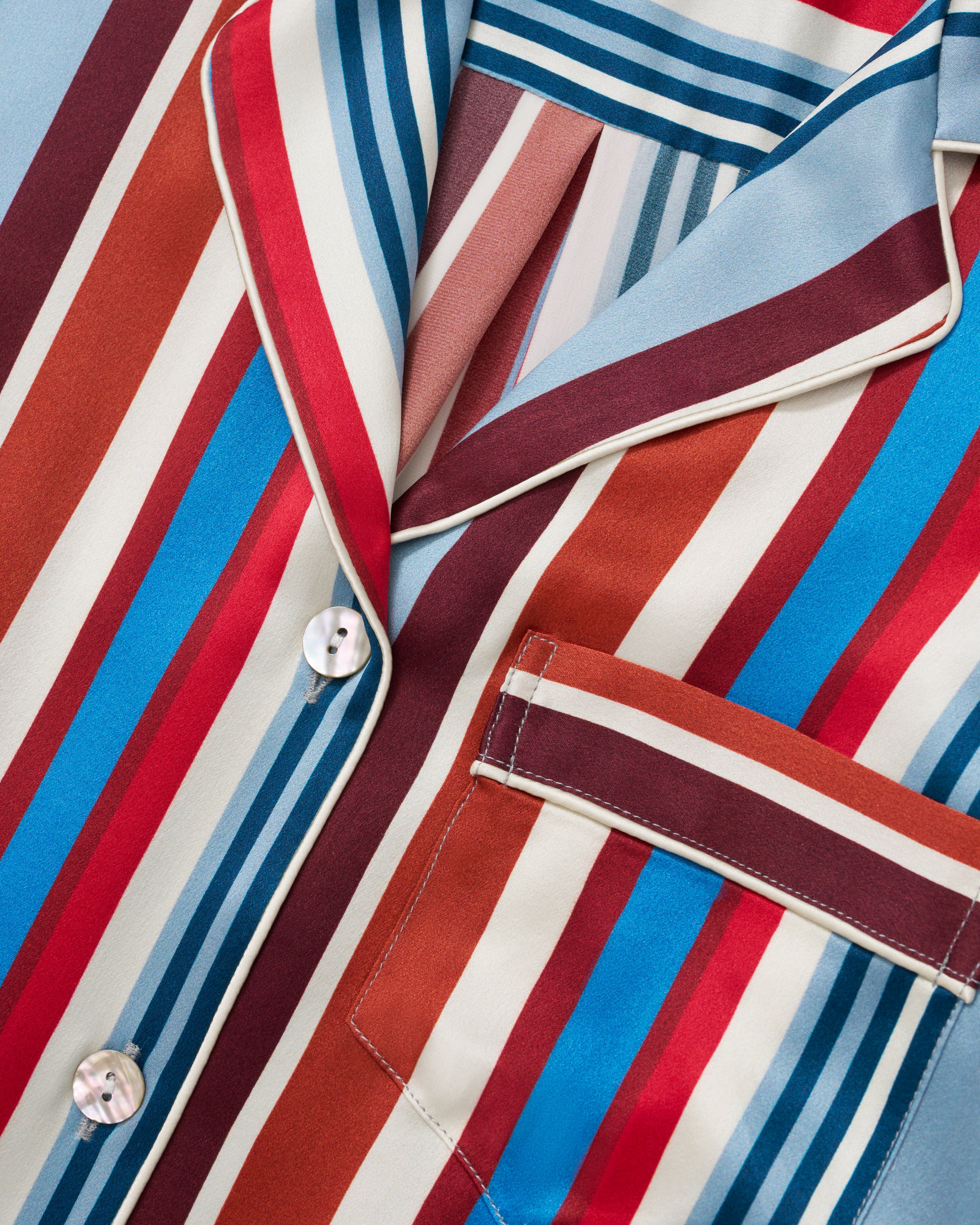The Women's Silk Short Set in Discovery Stripe features a short-sleeved button-up shirt and matching drawstring shorts with bold vertical stripes in red, blue, brown, and white.