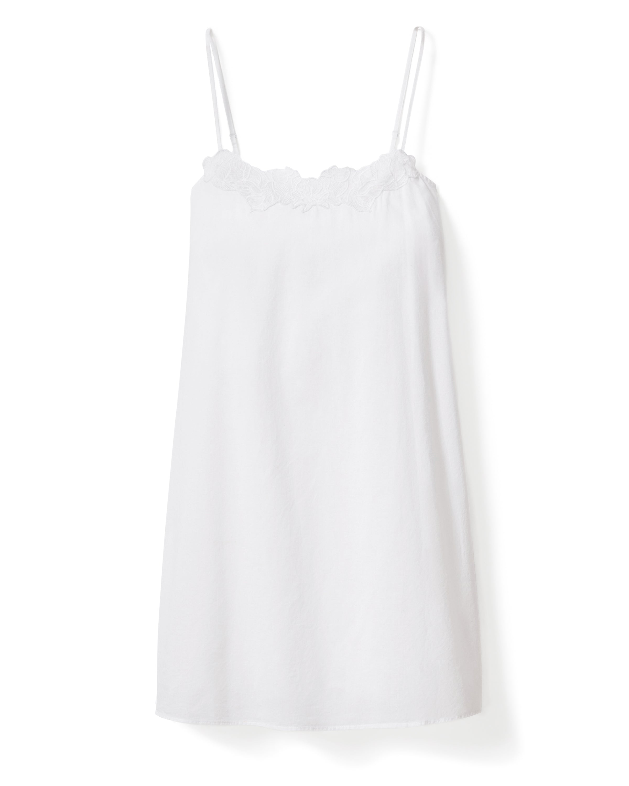 A woman with long, wavy hair stands barefoot against a plain light background, looking at the camera with a slight smile while wearing the Women's Voile Fleur Slip in White.