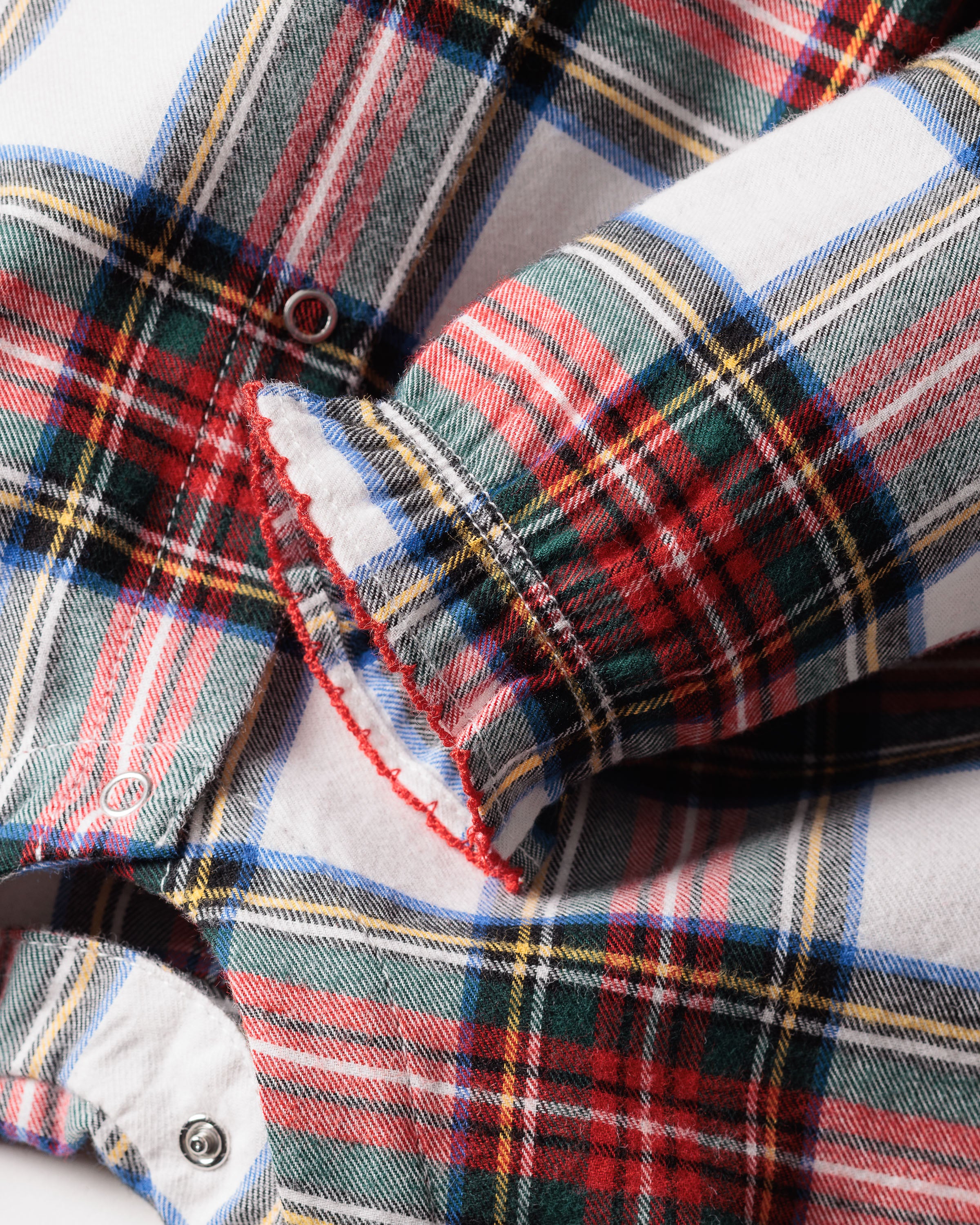 Close-up of Petite Plumes Babys Brushed Cotton Madeline Romper in Balmoral Tartan, featuring a red, white, blue, and green plaid. Focus on the sleeve with frayed cuff and button details. Made with chemical-free fabric for comfort and safety.