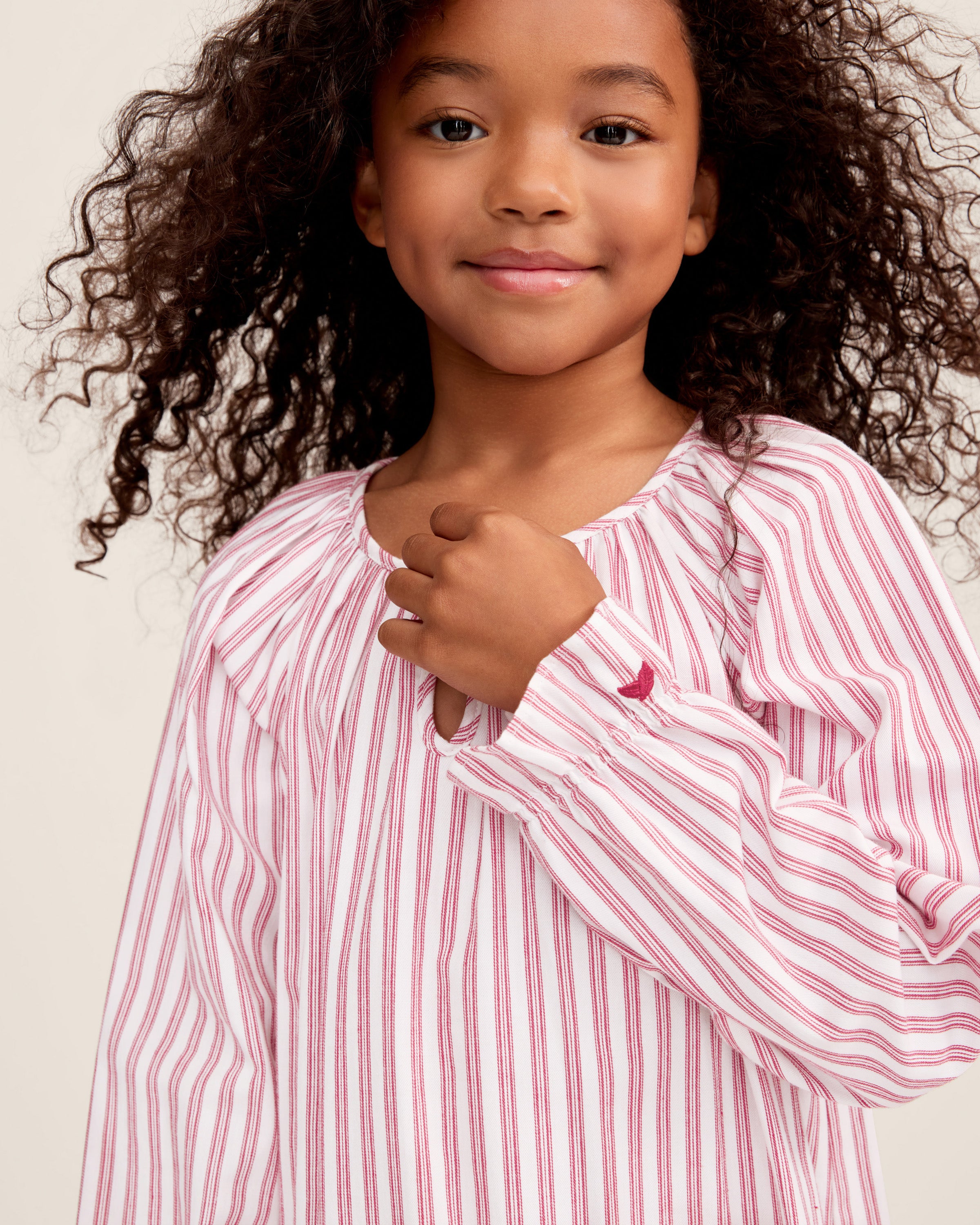 Close-up of Petite Plumes Girls Twill Delphine Nightgown in Antique Red Ticking, featuring pink and white stripes with red stitched ruffles and an embroidered star. Ideal for childrens sleepwear, its smooth texture highlights the detailed pattern and craftsmanship.
