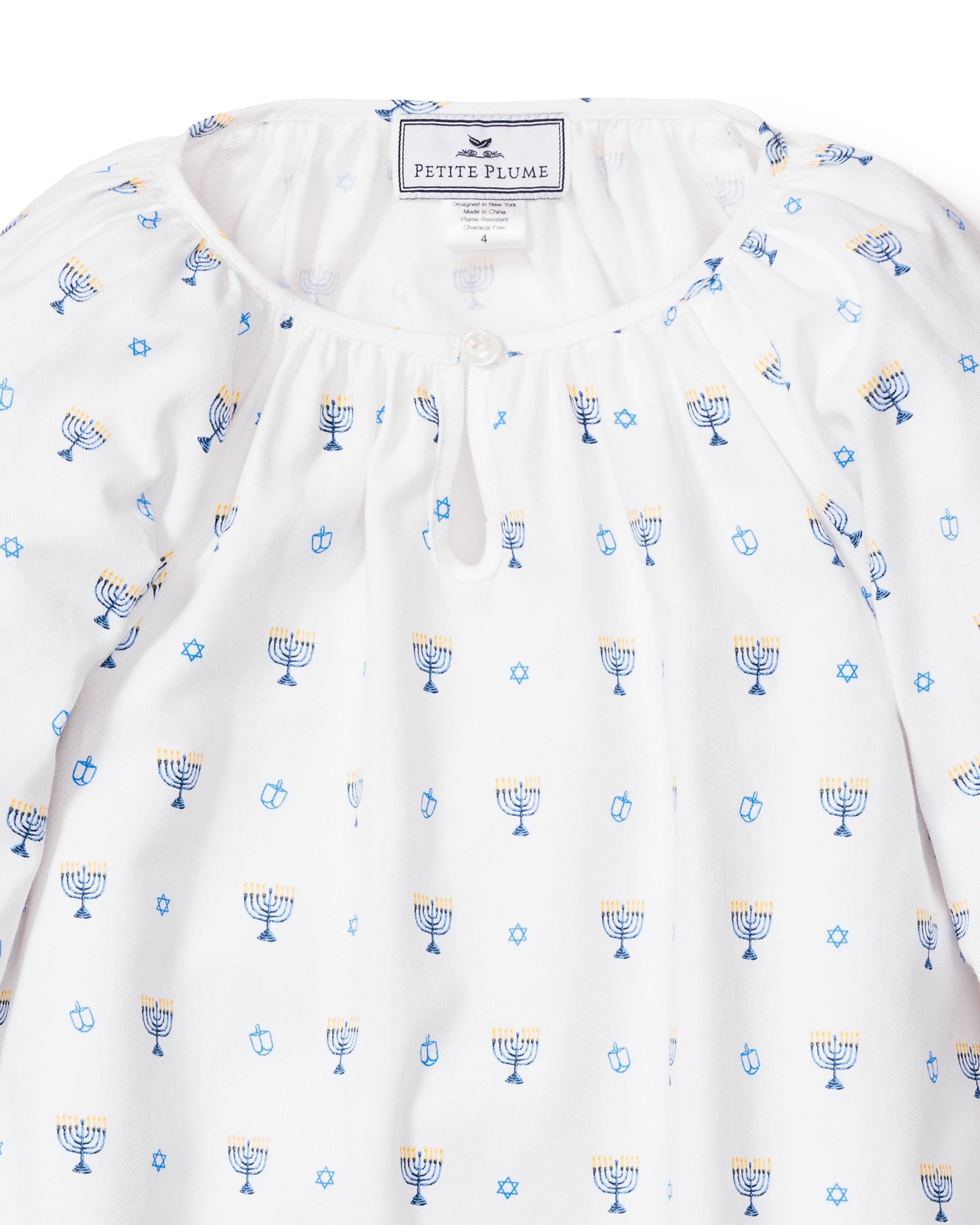 The Petite Plume Girls Twill Delphine Nightgown in Happy Hanukkah, adorned with blue and yellow menorahs, blue Stars of David, and dreidels, is perfect as childrens Hanukkah pajamas. It features a small button closure collar and a Petite Plume label inside the neckline.
