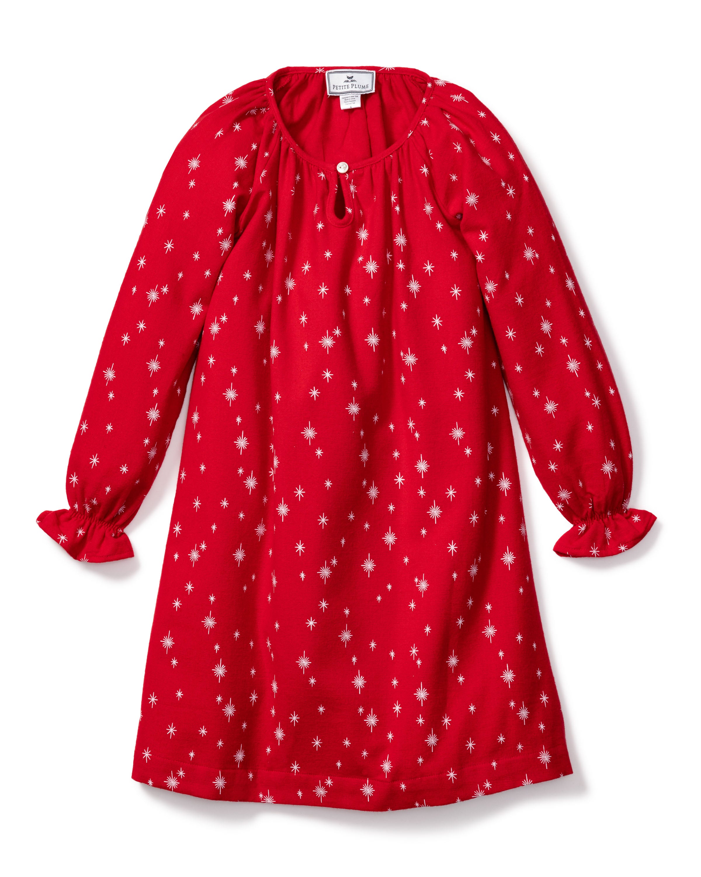 The Petite Plume Girls Flannel Delphine Nightgown in Starry Night features a red design with long sleeves, ruffled cuffs, and a round neckline adorned with white stars. Made from flame-retardant fabric, it has a button at the neck and is perfect for casual wear.