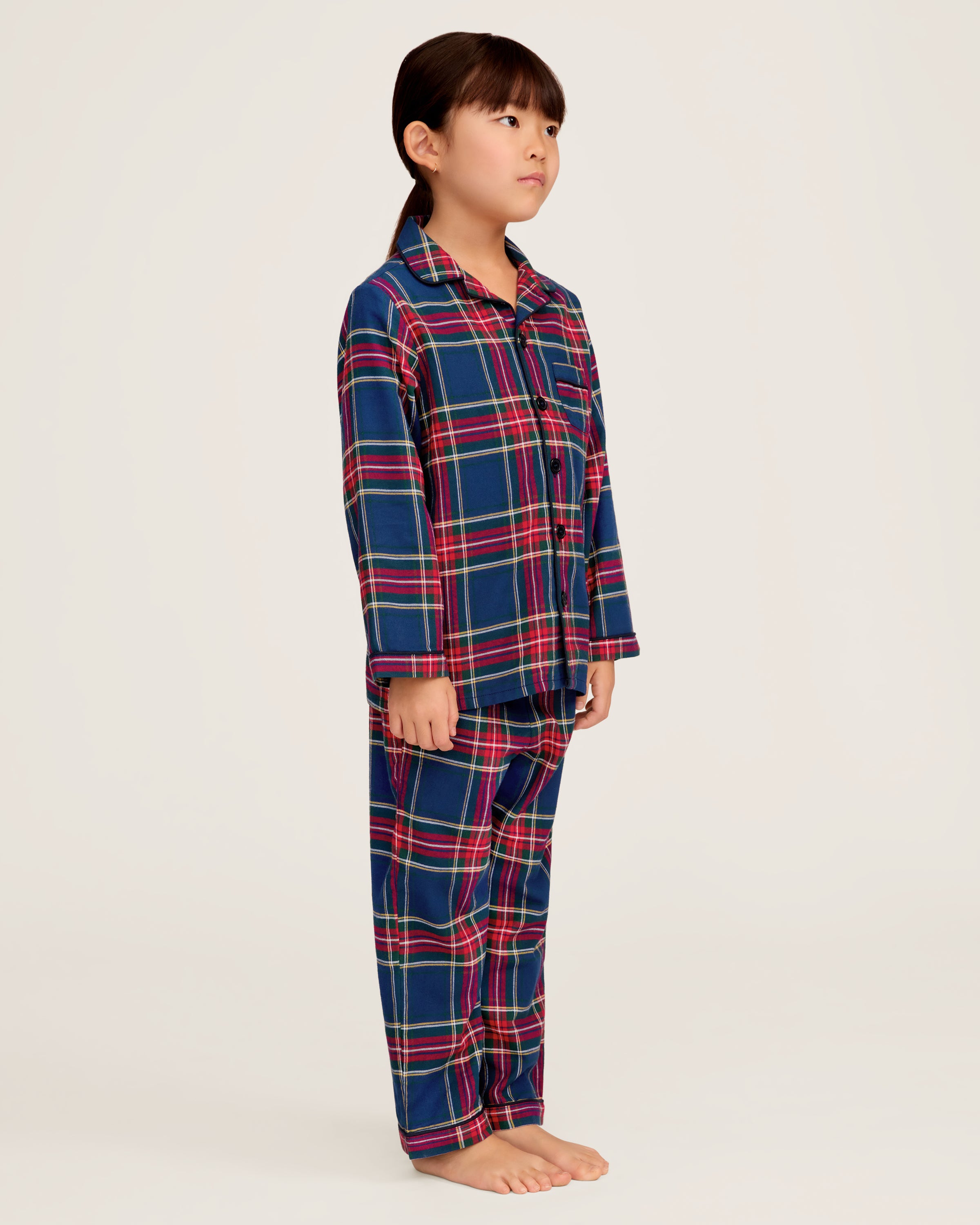 Close-up of a lavish Kids Brushed Cotton Pajama Set in Windsor Tartan by Petite Plume, showcasing red, blue, green, and yellow intersecting stripes forming squares and rectangles. A visible button and seam complete this classic pajama look.