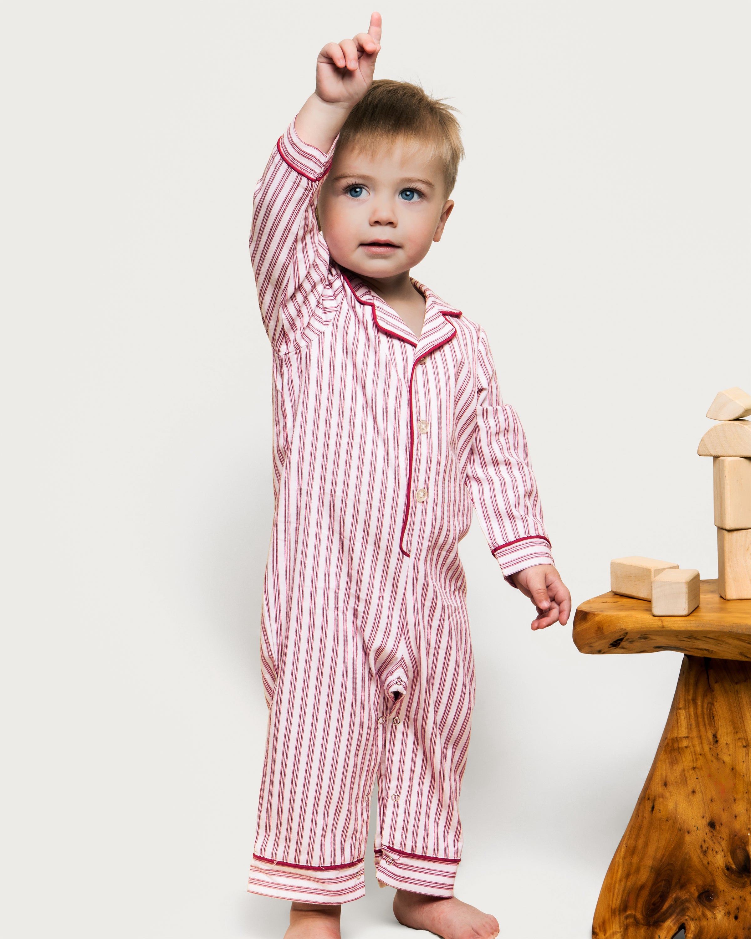 The Babys Twill Romper in Antique Red Ticking by Petite Plume is a childs long-sleeve jumpsuit with vertical red and white stripes, made from lightweight brushed twill. It features a collar, red trim on the cuffs and ankles, and a back flap pocket.